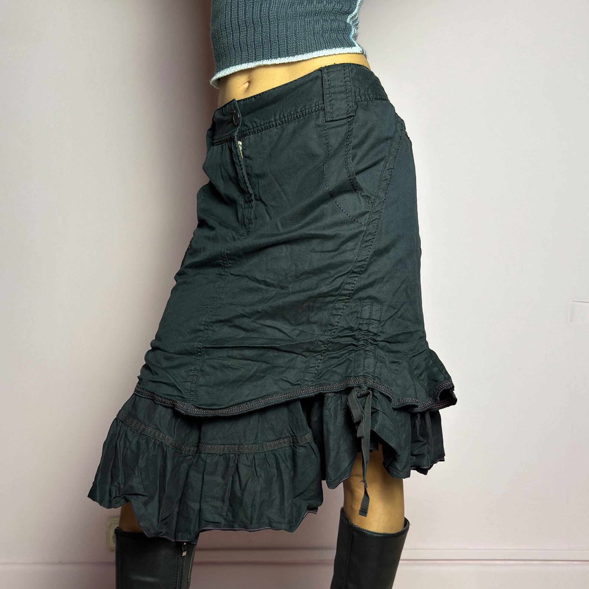 The Y2K Black Layered Skirt by Marithé François Girbaud is a vintage 2000s statement piece featuring a structured design with ruched details and ruffled layers for added texture and movement. Designed with a mid-rise fit, button and zipper closure, embroidered side detail, and an asymmetrical hem, this skirt blends edgy streetwear vibes with a playful, gothic aesthetic. Perfect for casual grunge and alternative looks. adult world shop