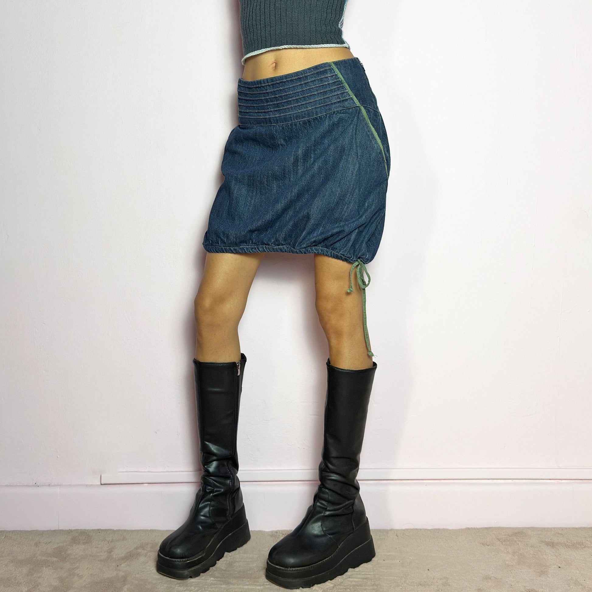 The Y2K Denim Bubble Mini Skirt is a vintage 2000s piece featuring a dark wash denim with unique structured pleating at the waist. Designed with an adjustable bubble hem with drawstrings for a customizable fit, this skirt blends playful and edgy aesthetics. It also includes a side zipper closure. Perfect for statement streetwear looks. adult world shop