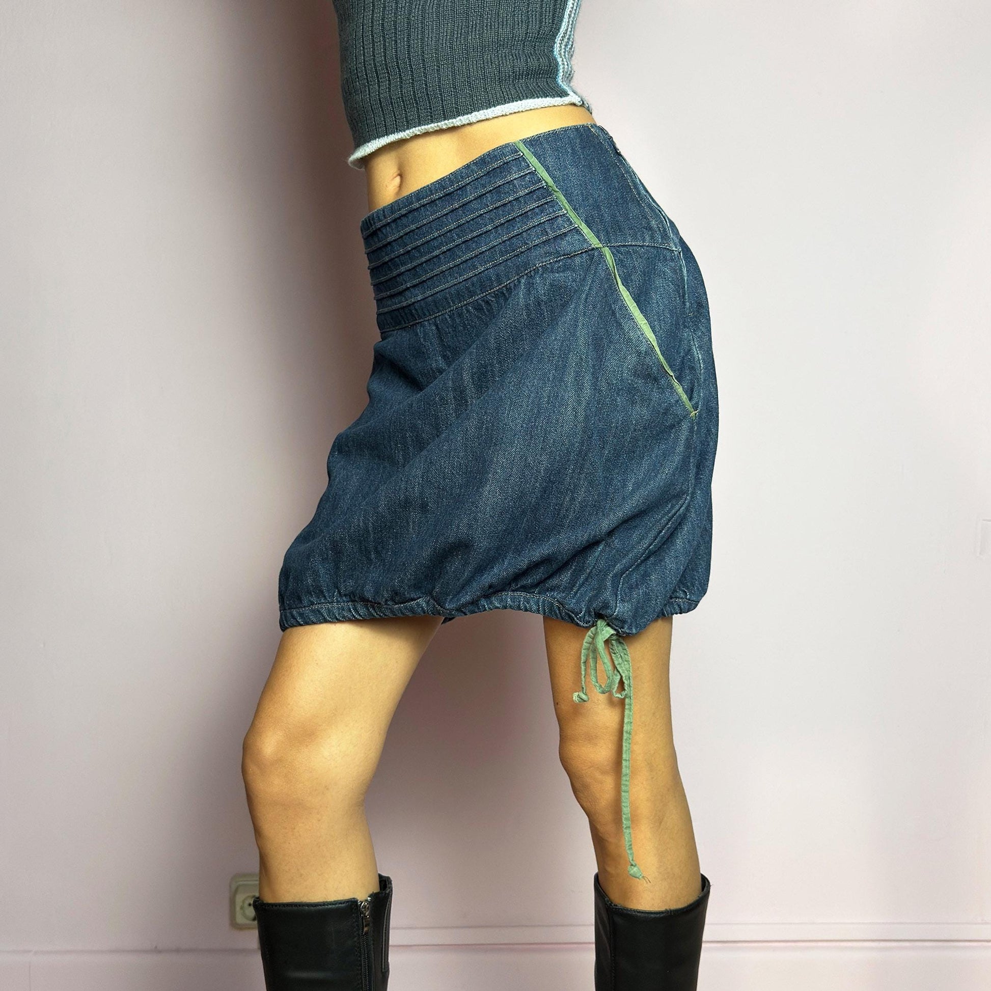 The Y2K Denim Bubble Mini Skirt is a vintage 2000s piece featuring a dark wash denim with unique structured pleating at the waist. Designed with an adjustable bubble hem with drawstrings for a customizable fit, this skirt blends playful and edgy aesthetics. It also includes a side zipper closure. Perfect for statement streetwear looks. adult world shop