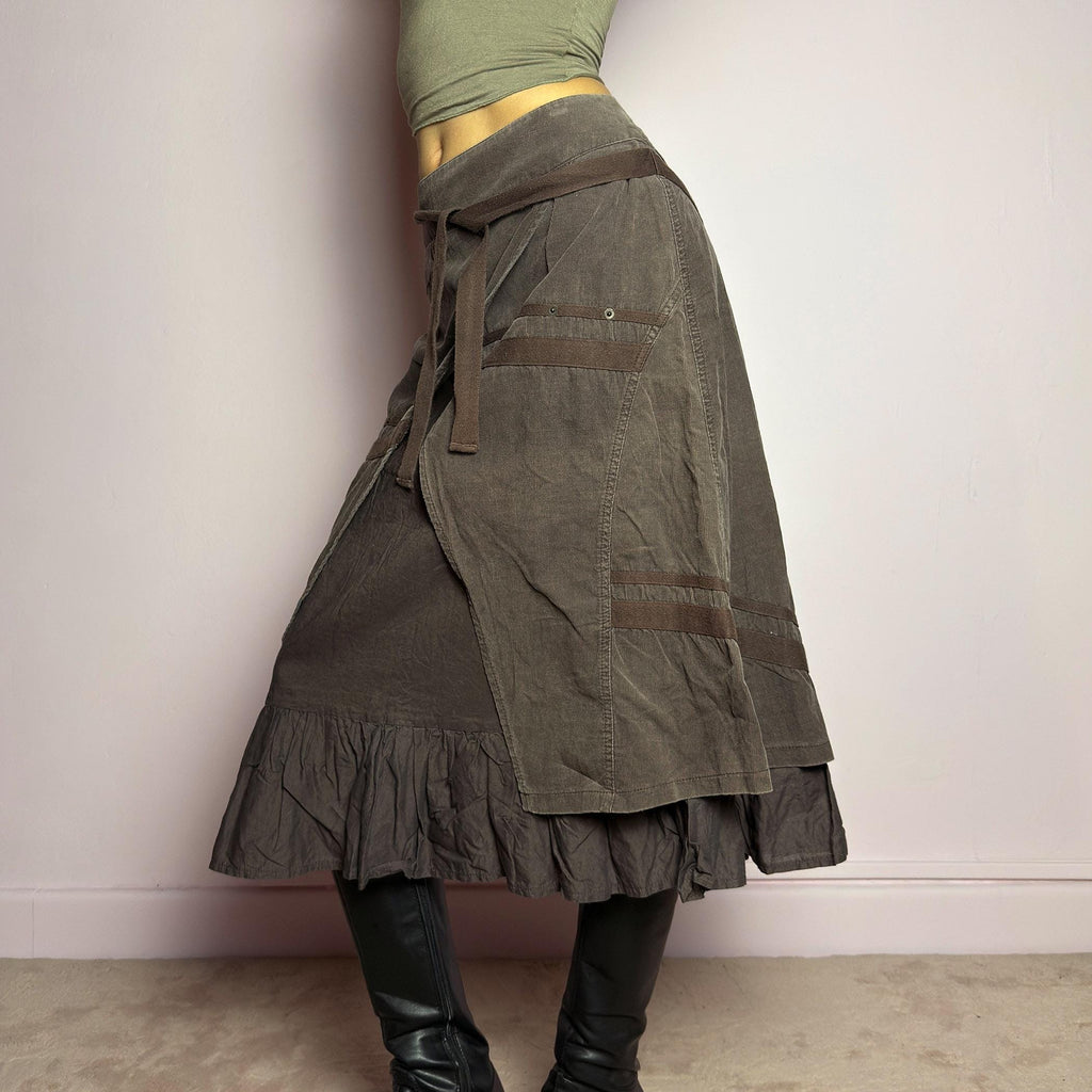 The Y2K Layered Brown Midi Skirt is a unique vintage 2000s piece featuring an asymmetric wrap design with a layered ruffle hem. Made from corduroy-cotton fabric, it includes tie closures for an adjustable fit, a back zipper closure, and subtle stitched detailing that adds a deconstructed touch. Perfect for earthy, bohemian, or avant-garde styling. adult world shop