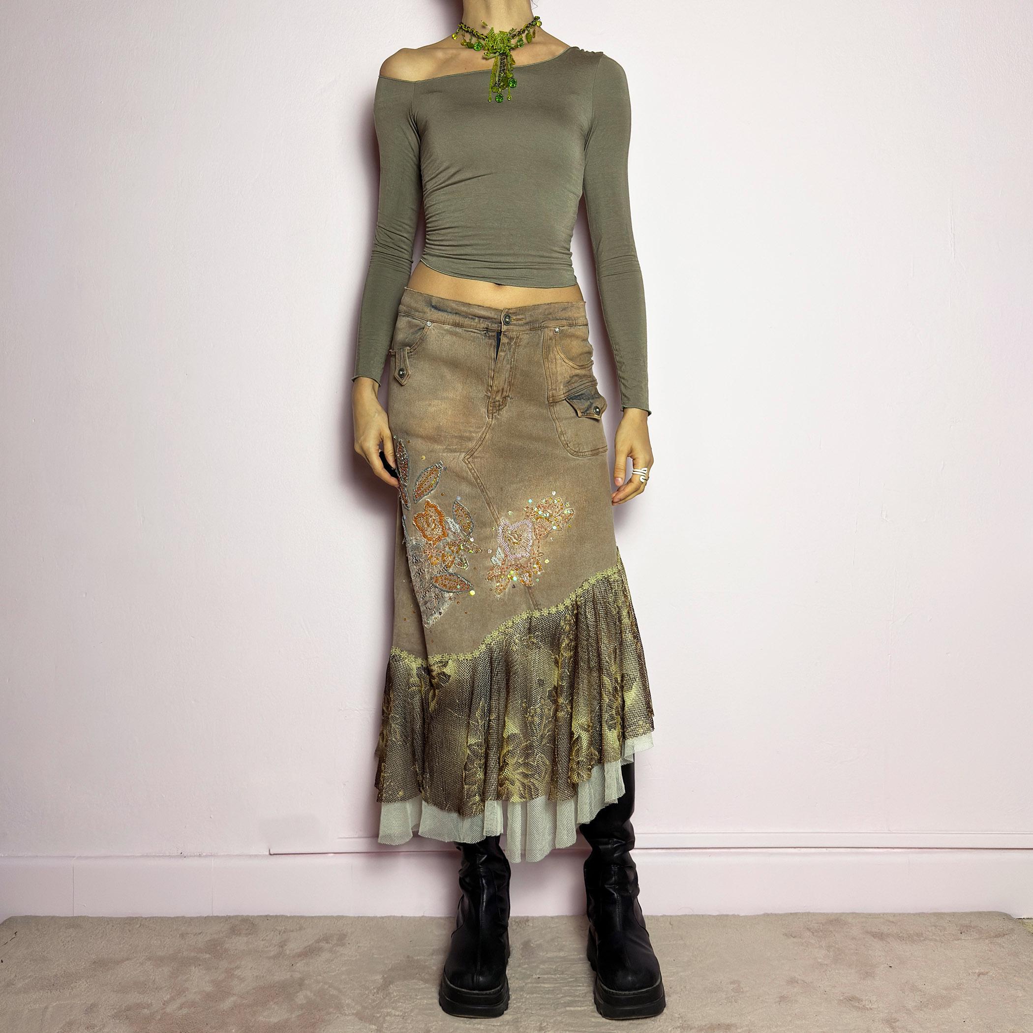 The Y2K Asymmetric Ruffle Midi Skirt is a vintage 2000s statement piece featuring a stretchy distressed tan denim base adorned with intricate beaded floral embroidery and sequin details. Designed with an asymmetric layered ruffle hem made of sheer lace and mesh with a metallic floral pattern, this skirt creates a dreamy, deconstructed aesthetic. It includes a button and zipper closure, belt loops, and pockets. adult world shop
