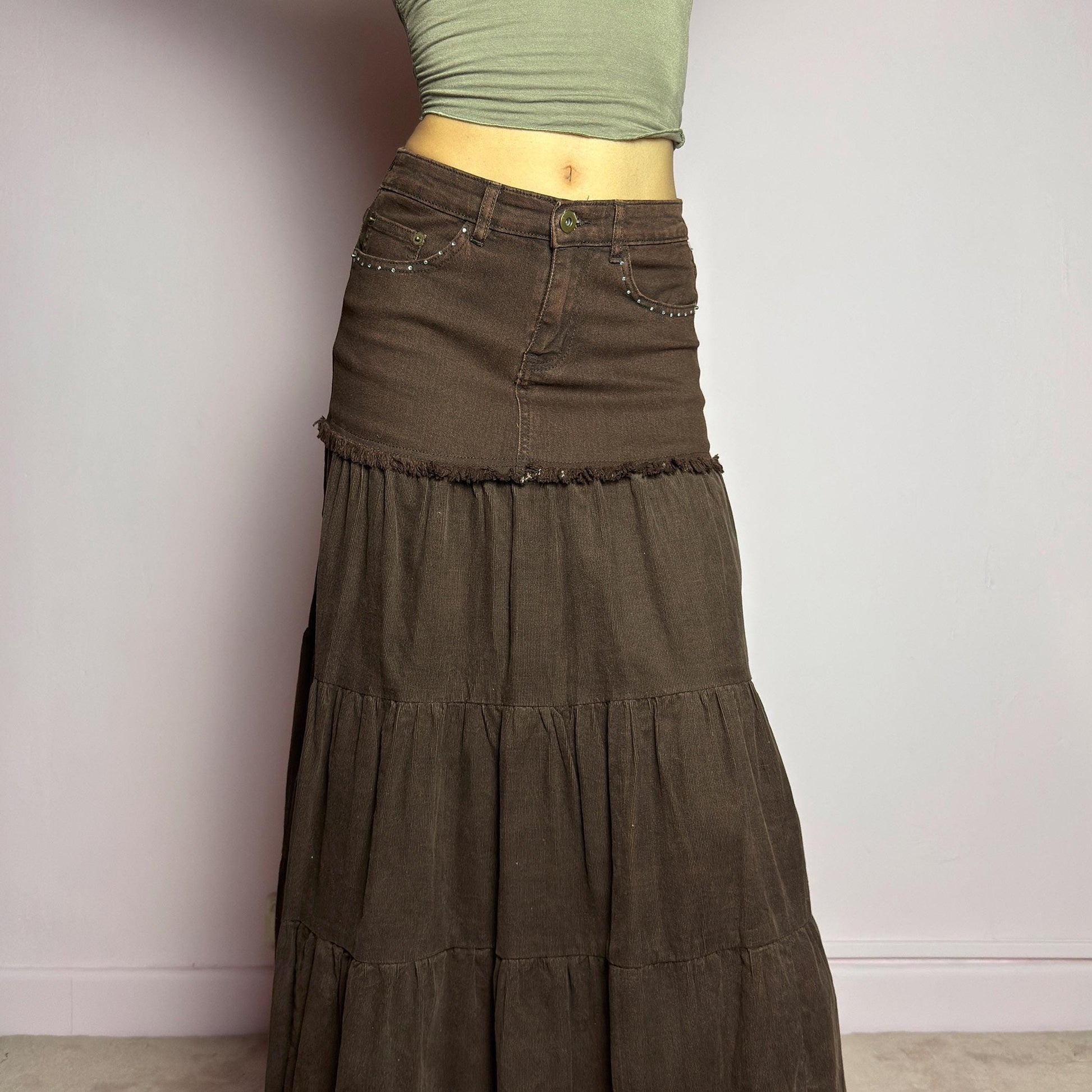 The Y2K Brown Tiered Midi Skirt is a vintage 2000s piece combining denim and soft corduroy for a unique mixed-fabric look. Featuring a stretchy waistband with rhinestone embellishments, pockets and a button-zipper closure, this skirt transitions into flowy tiered corduroy panels for a boho-inspired silhouette. Perfect for casual outfits. adult world shop