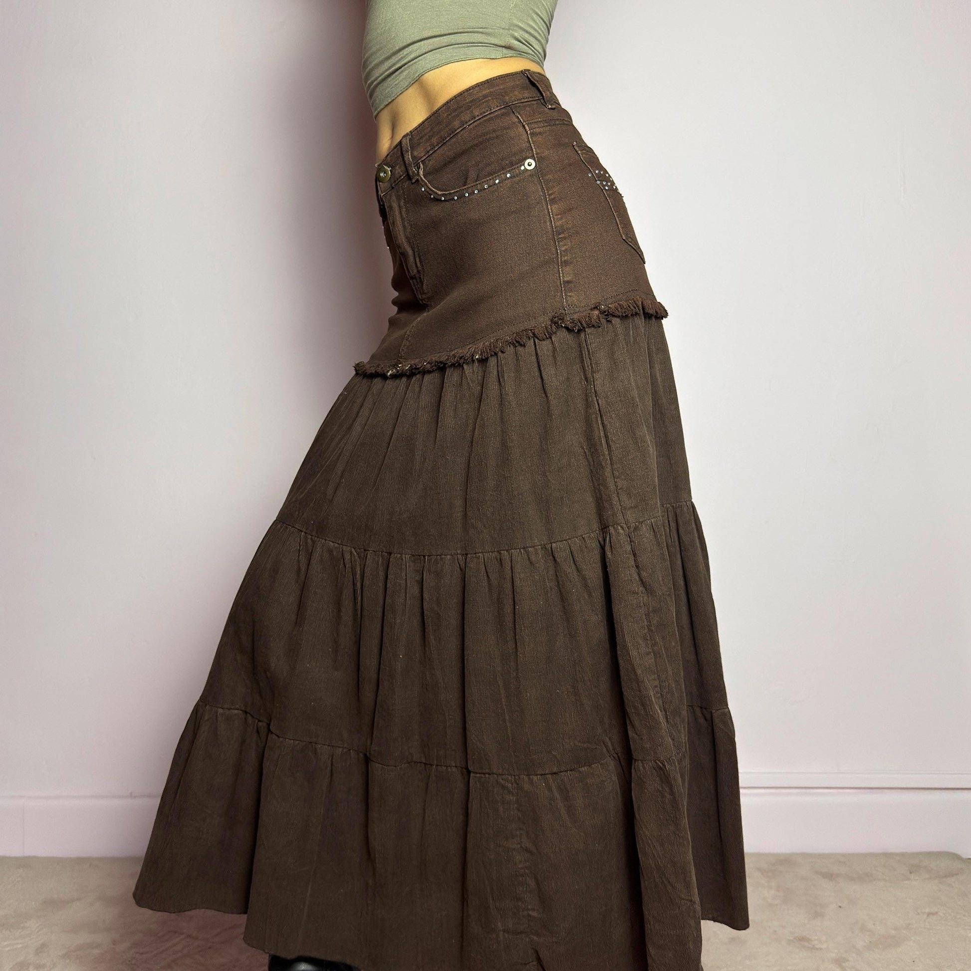 The Y2K Brown Tiered Midi Skirt is a vintage 2000s piece combining denim and soft corduroy for a unique mixed-fabric look. Featuring a stretchy waistband with rhinestone embellishments, pockets and a button-zipper closure, this skirt transitions into flowy tiered corduroy panels for a boho-inspired silhouette. Perfect for casual outfits. adult world shop