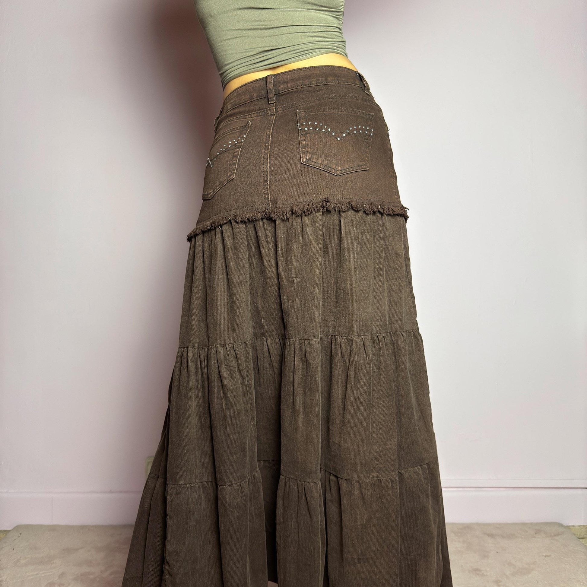 The Y2K Brown Tiered Midi Skirt is a vintage 2000s piece combining denim and soft corduroy for a unique mixed-fabric look. Featuring a stretchy waistband with rhinestone embellishments, pockets and a button-zipper closure, this skirt transitions into flowy tiered corduroy panels for a boho-inspired silhouette. Perfect for casual outfits. adult world shop