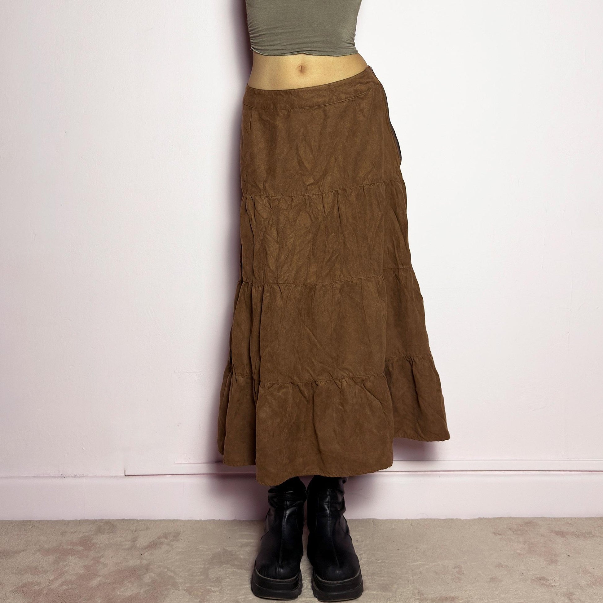 The Y2K Tiered Brown Midi Skirt is a vintage 2000s piece featuring a soft faux suede style fabric. Designed with a voluminous tiered structure for a flowy silhouette and a side zipper closure, this skirt has a mid-rise fit and an earthy brown tone, perfect for bohemian or casual outfits. adult world shop