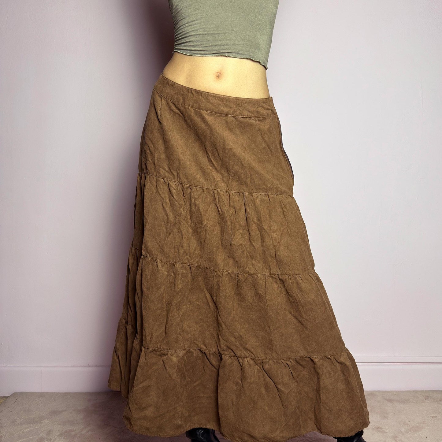 The Y2K Tiered Brown Midi Skirt is a vintage 2000s piece featuring a soft faux suede style fabric. Designed with a voluminous tiered structure for a flowy silhouette and a side zipper closure, this skirt has a mid-rise fit and an earthy brown tone, perfect for bohemian or casual outfits. adult world shop