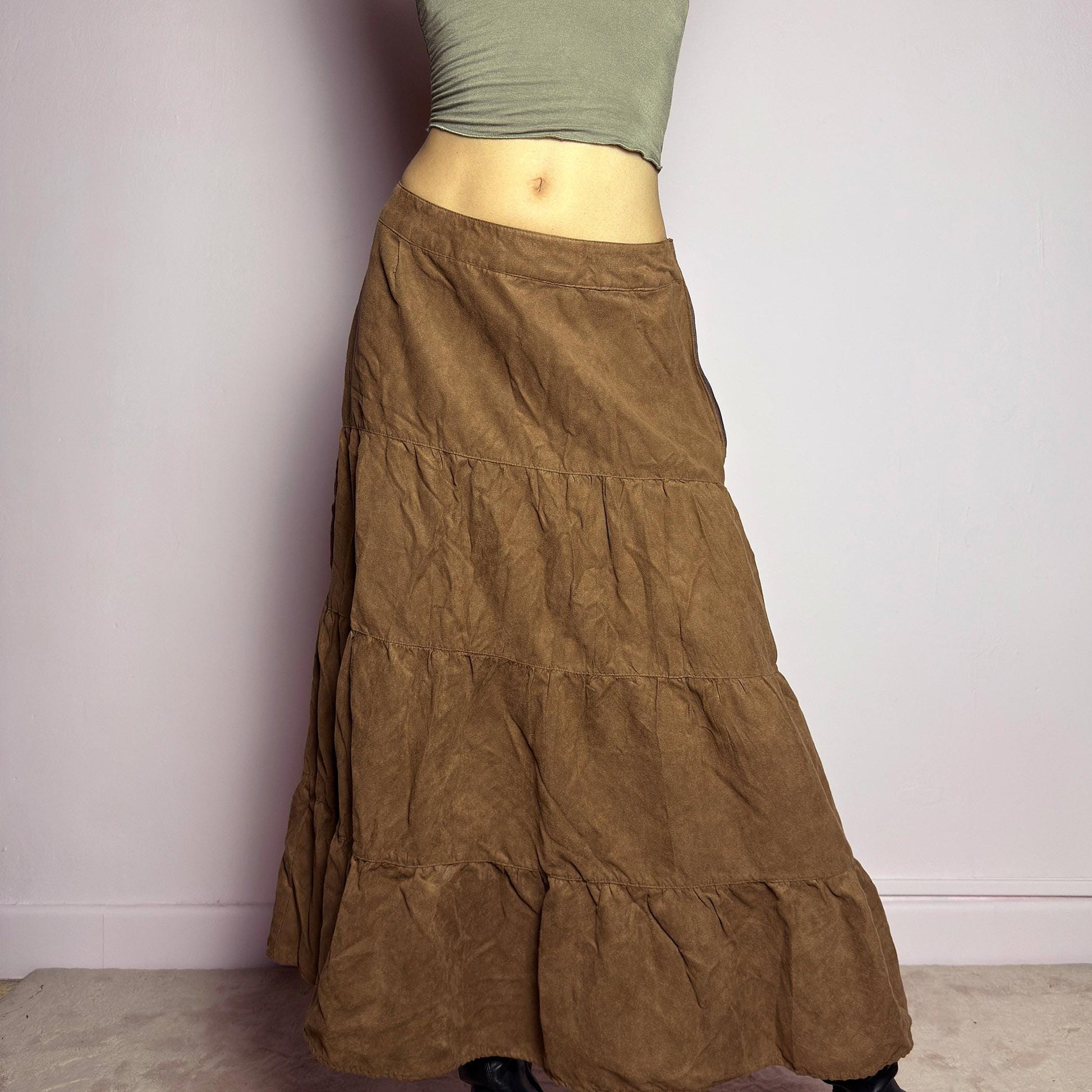 The Y2K Tiered Brown Midi Skirt is a vintage 2000s piece featuring a soft faux suede style fabric. Designed with a voluminous tiered structure for a flowy silhouette and a side zipper closure, this skirt has a mid-rise fit and an earthy brown tone, perfect for bohemian or casual outfits. adult world shop