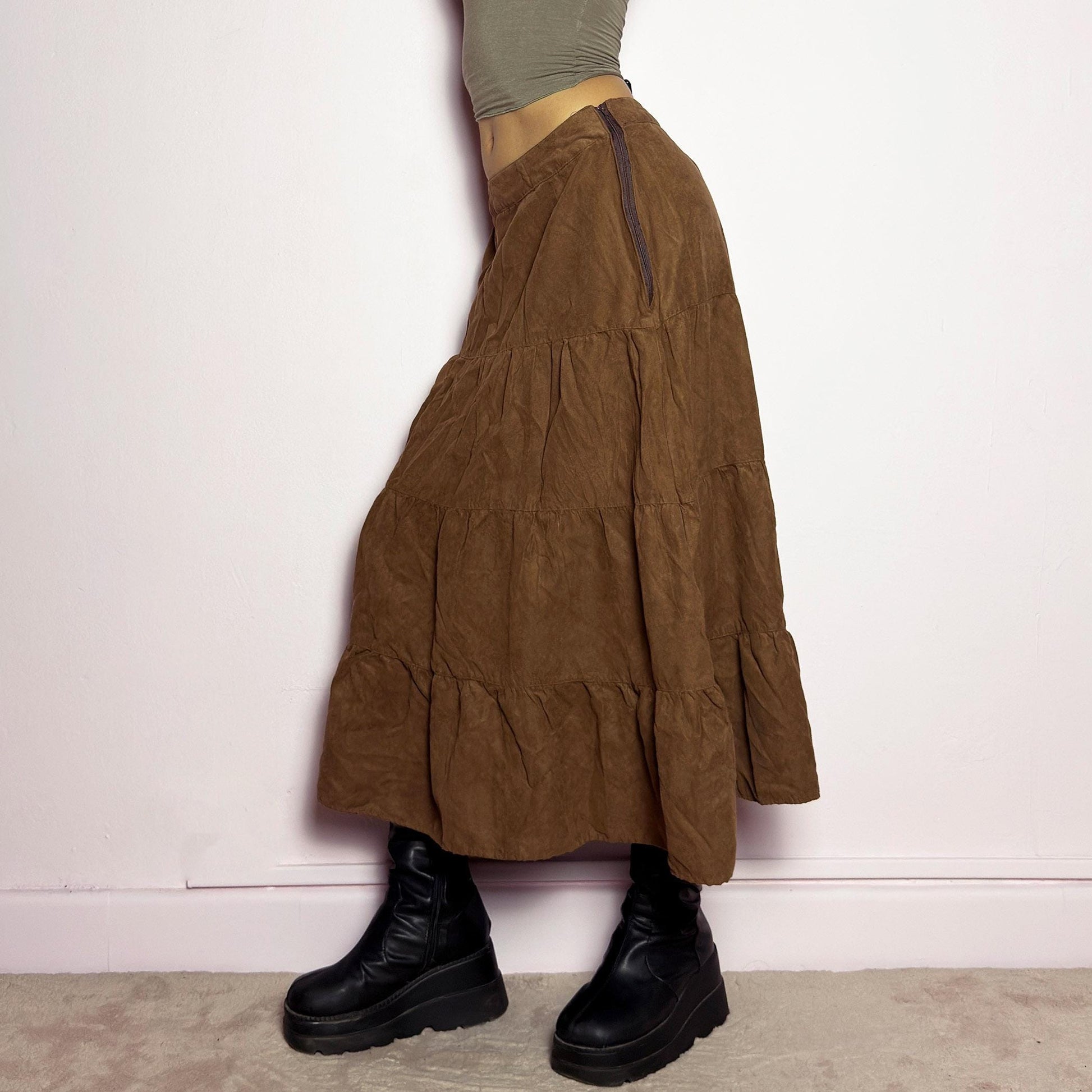 The Y2K Tiered Brown Midi Skirt is a vintage 2000s piece featuring a soft faux suede style fabric. Designed with a voluminous tiered structure for a flowy silhouette and a side zipper closure, this skirt has a mid-rise fit and an earthy brown tone, perfect for bohemian or casual outfits. adult world shop