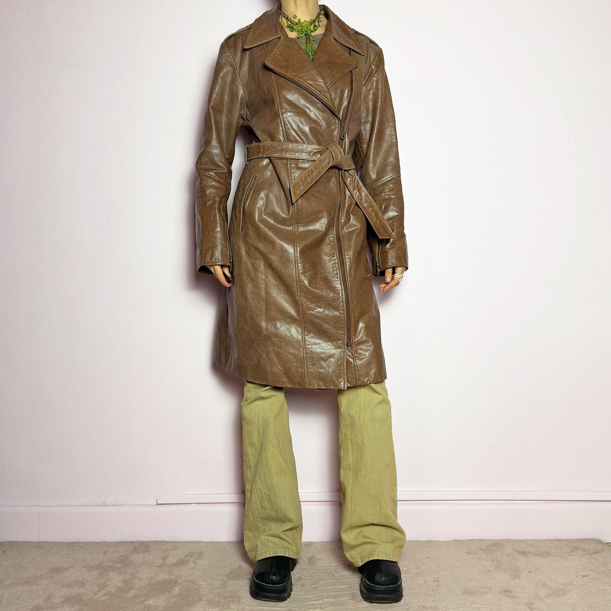 The Y2K Long Brown Leather Coat is a heavy, structured vintage 2000s piece crafted from genuine leather. It features an asymmetrical zip closure, a wide lapel collar, and a belted waist for a cinched silhouette. The coat includes pockets and a smooth lining for comfort. With its durable construction and timeless design, this vintage long leather coat is perfect for edgy streetwear or sophisticated layering. adult world shop