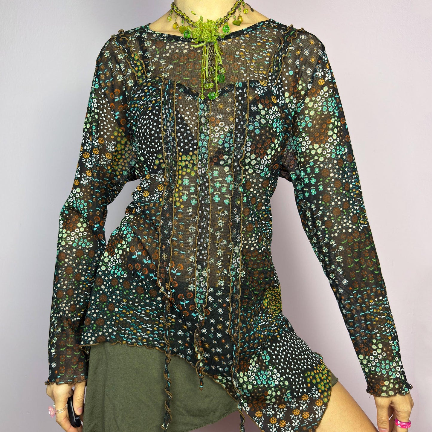 The Y2K Black Asymmetric Mesh Top is a vintage 2000s statement piece featuring semi-sheer mesh fabric with a floral and geometric print. Designed with an edgy asymmetric cut and delicate lettuce hem detailing, this top embodies a deconstructed aesthetic with a fairy grunge-inspired touch. The lightweight, stretchy fabric makes it perfect for layering, making it an ideal choice for summer avant-garde outfits. adult world shop