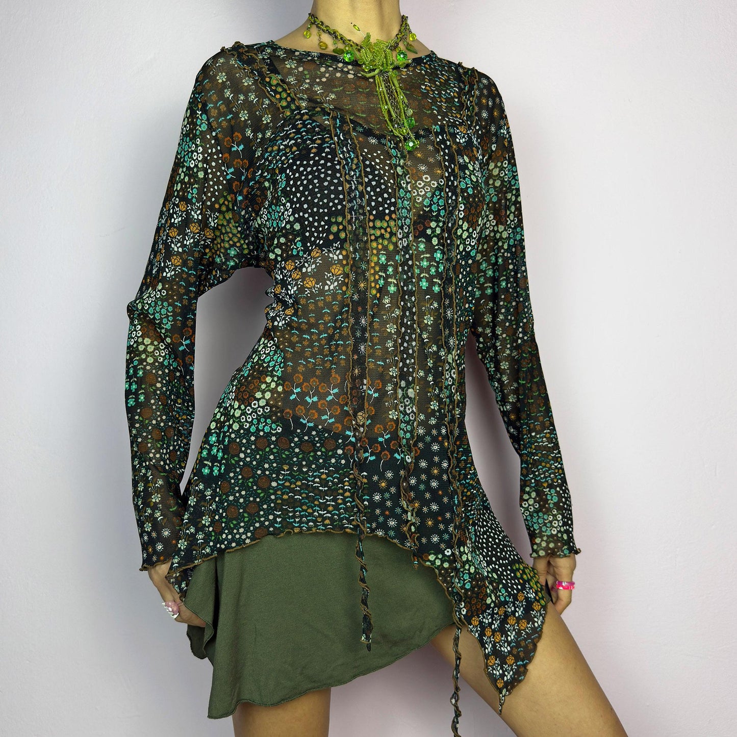 The Y2K Black Asymmetric Mesh Top is a vintage 2000s statement piece featuring semi-sheer mesh fabric with a floral and geometric print. Designed with an edgy asymmetric cut and delicate lettuce hem detailing, this top embodies a deconstructed aesthetic with a fairy grunge-inspired touch. The lightweight, stretchy fabric makes it perfect for layering, making it an ideal choice for summer avant-garde outfits. adult world shop
