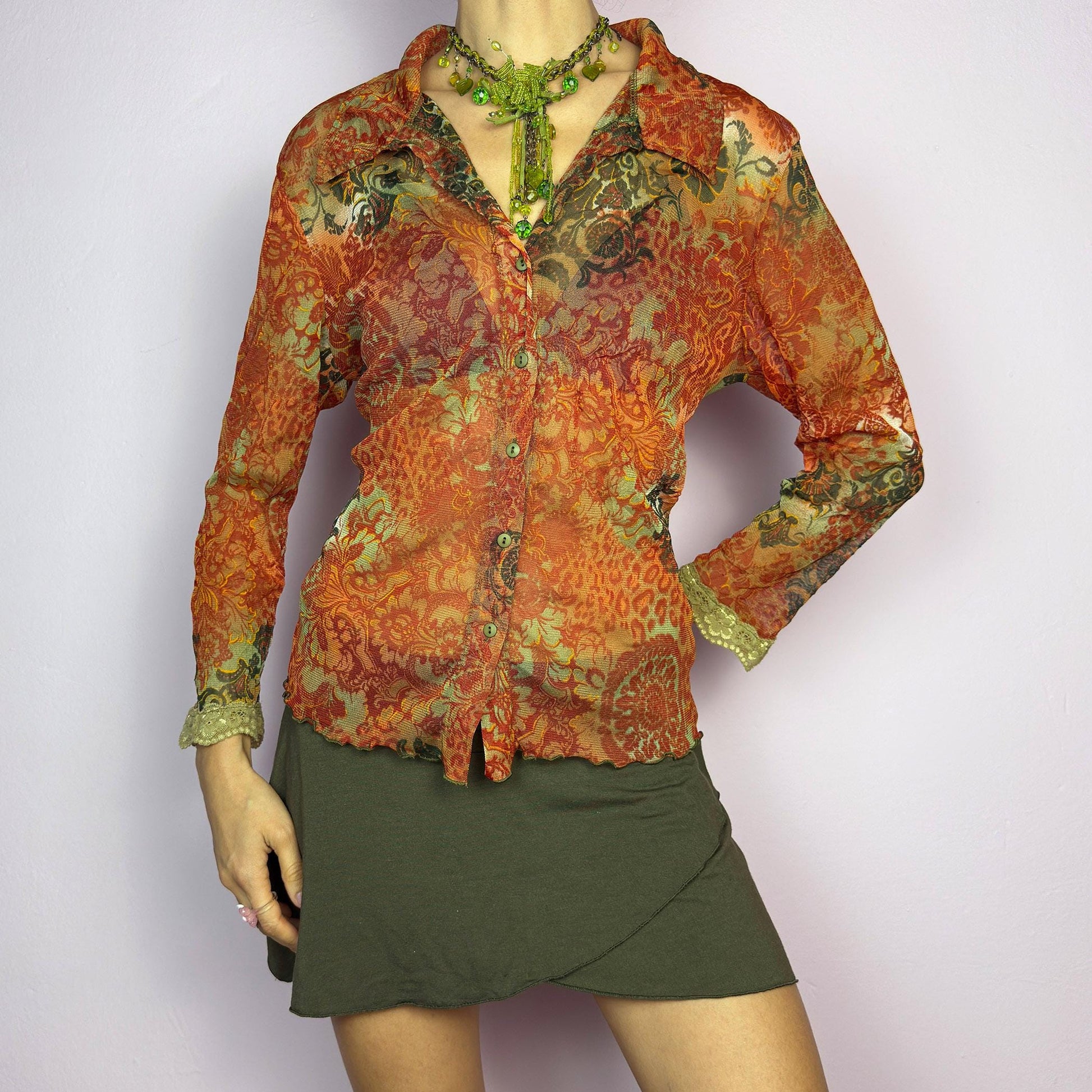 The Y2K Baroque Print Mesh Blouse is a vintage 2000s piece featuring a semi-sheer mesh fabric with a rich baroque-inspired floral print in warm tones. Designed with a fitted silhouette, button-up front, delicate lace trim on the cuffs and three quarter sleeves, the lightweight and stretchy fabric make it ideal for summer bohemian-inspired looks. adult world shop
