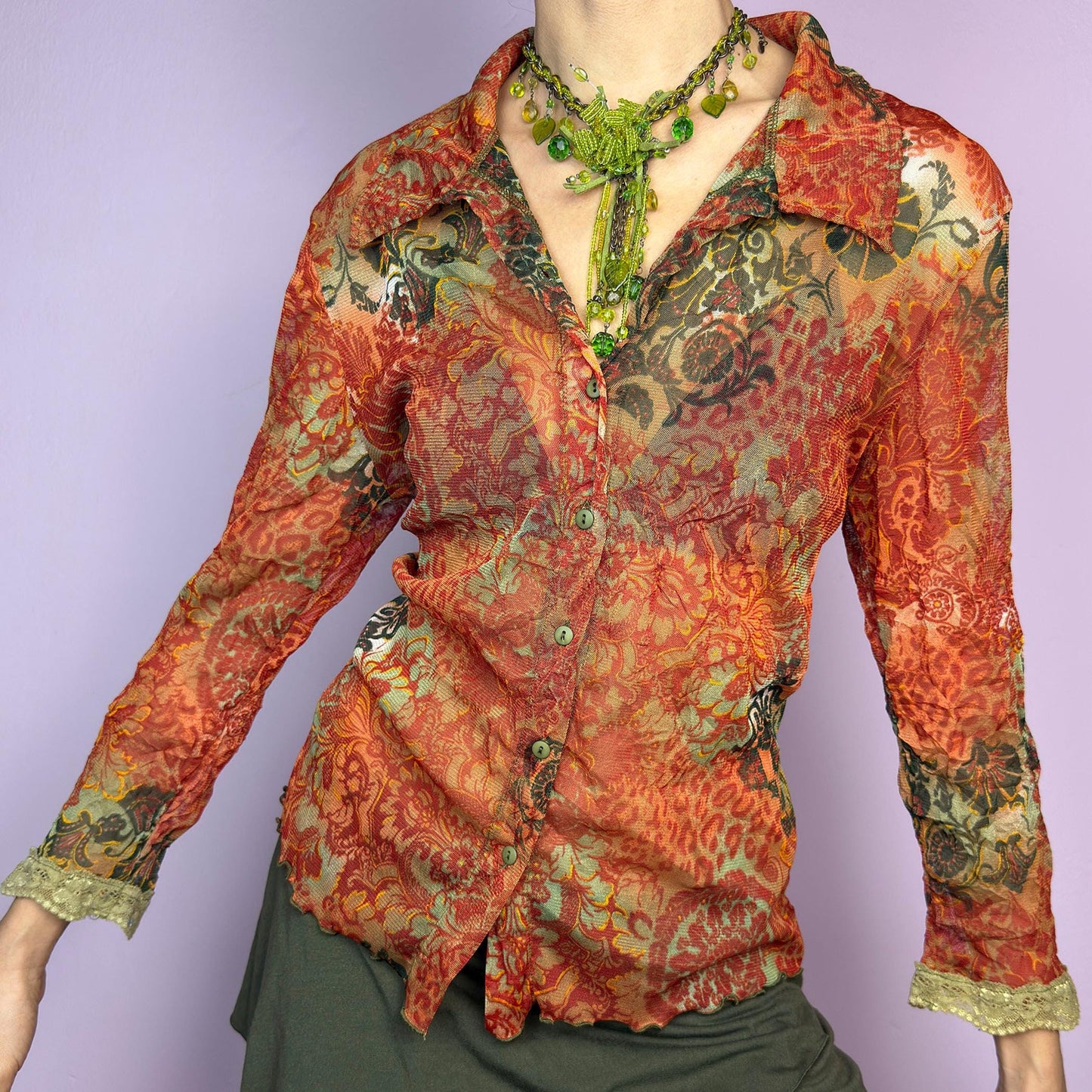 The Y2K Baroque Print Mesh Blouse is a vintage 2000s piece featuring a semi-sheer mesh fabric with a rich baroque-inspired floral print in warm tones. Designed with a fitted silhouette, button-up front, delicate lace trim on the cuffs and three quarter sleeves, the lightweight and stretchy fabric make it ideal for summer bohemian-inspired looks. adult world shop