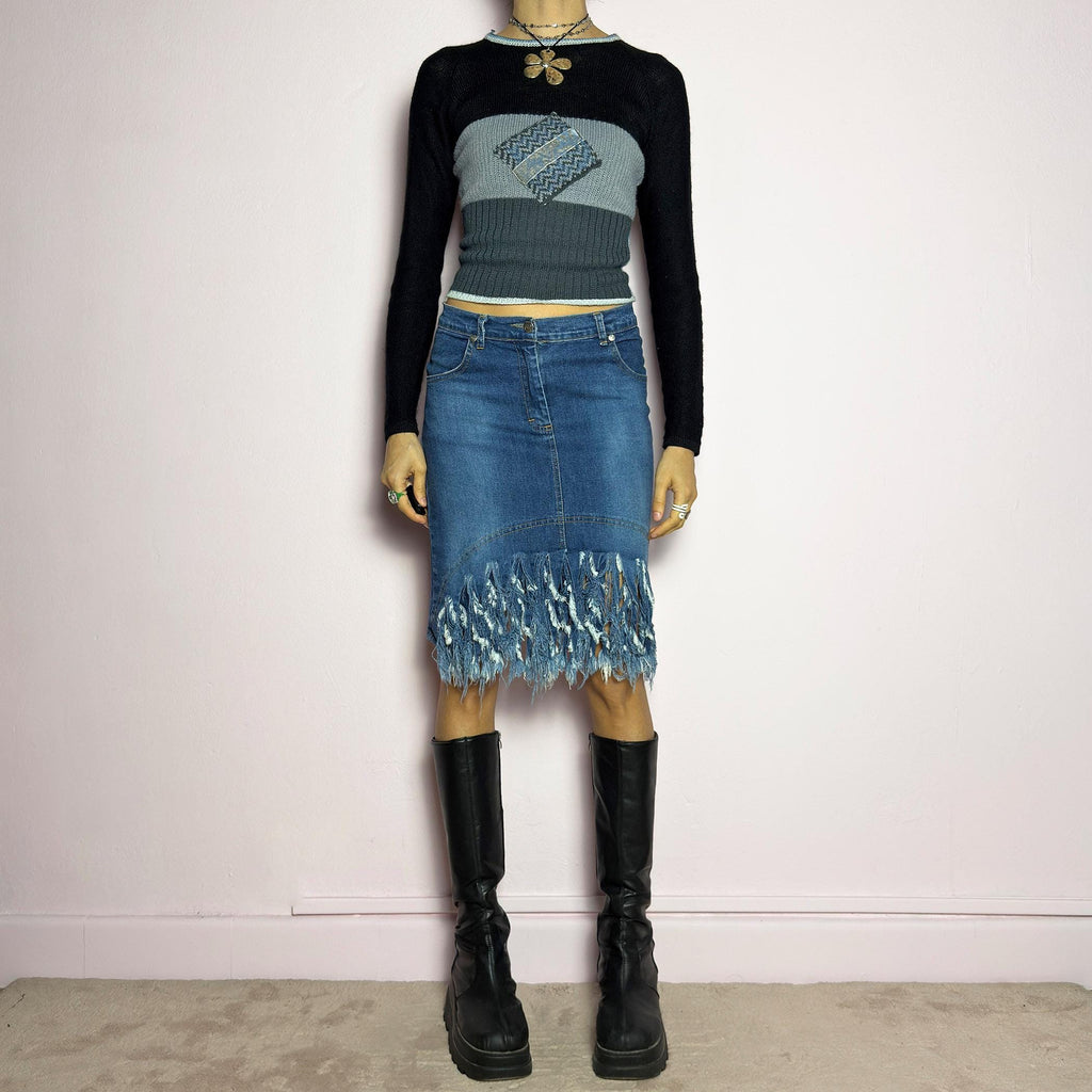 The Y2K Denim Distressed Midi Skirt is a vintage 2000s statement piece featuring a deconstructed look with dramatic distressed fringe details along the hem and back pockets. Designed with a stretchy structured denim fabric, a mid-rise fit, button and zipper closure, and pockets, this skirt blends edgy and casual aesthetics. adult world shop