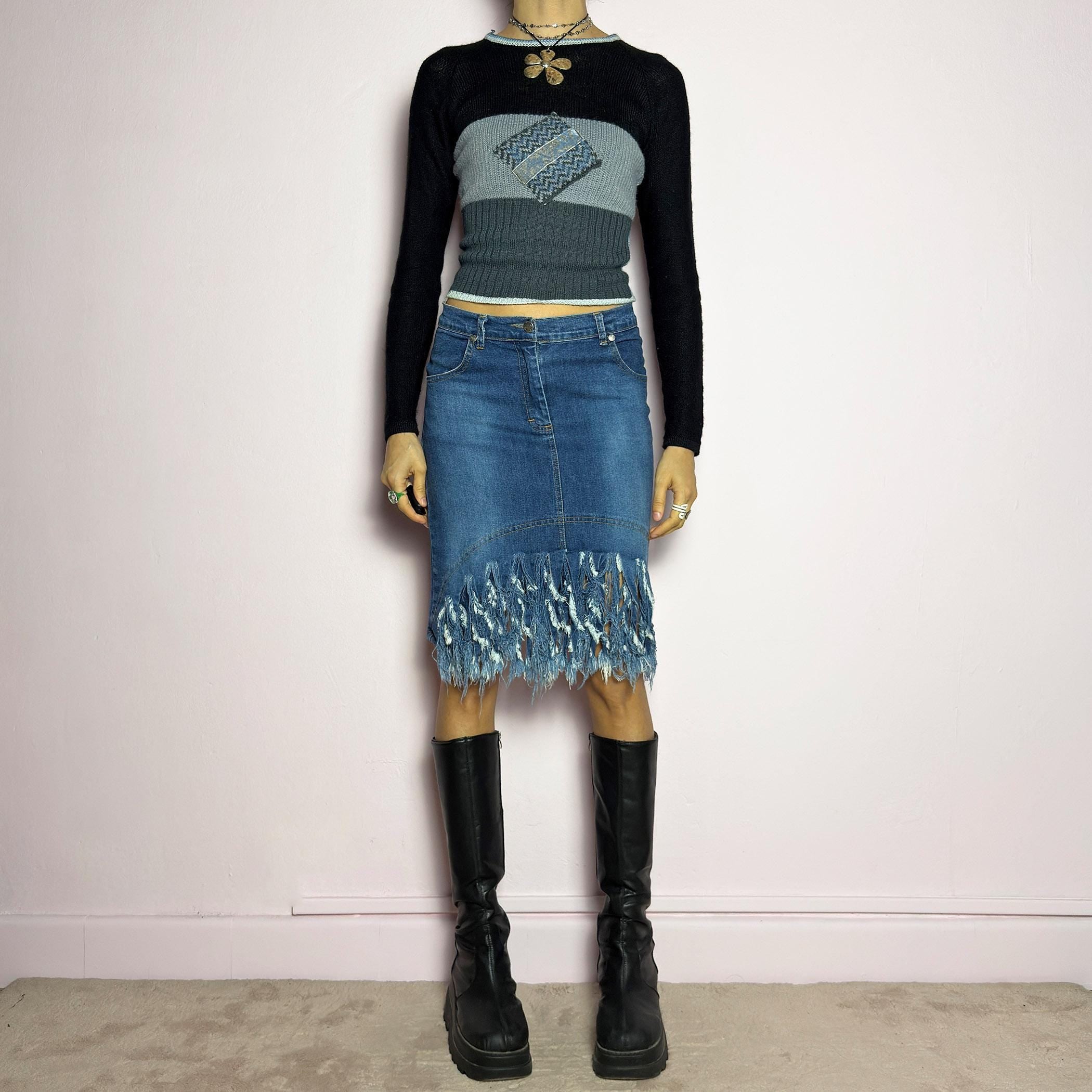 The Y2K Denim Distressed Midi Skirt is a vintage 2000s statement piece featuring a deconstructed look with dramatic distressed fringe details along the hem and back pockets. Designed with a stretchy structured denim fabric, a mid-rise fit, button and zipper closure, and pockets, this skirt blends edgy and casual aesthetics. adult world shop