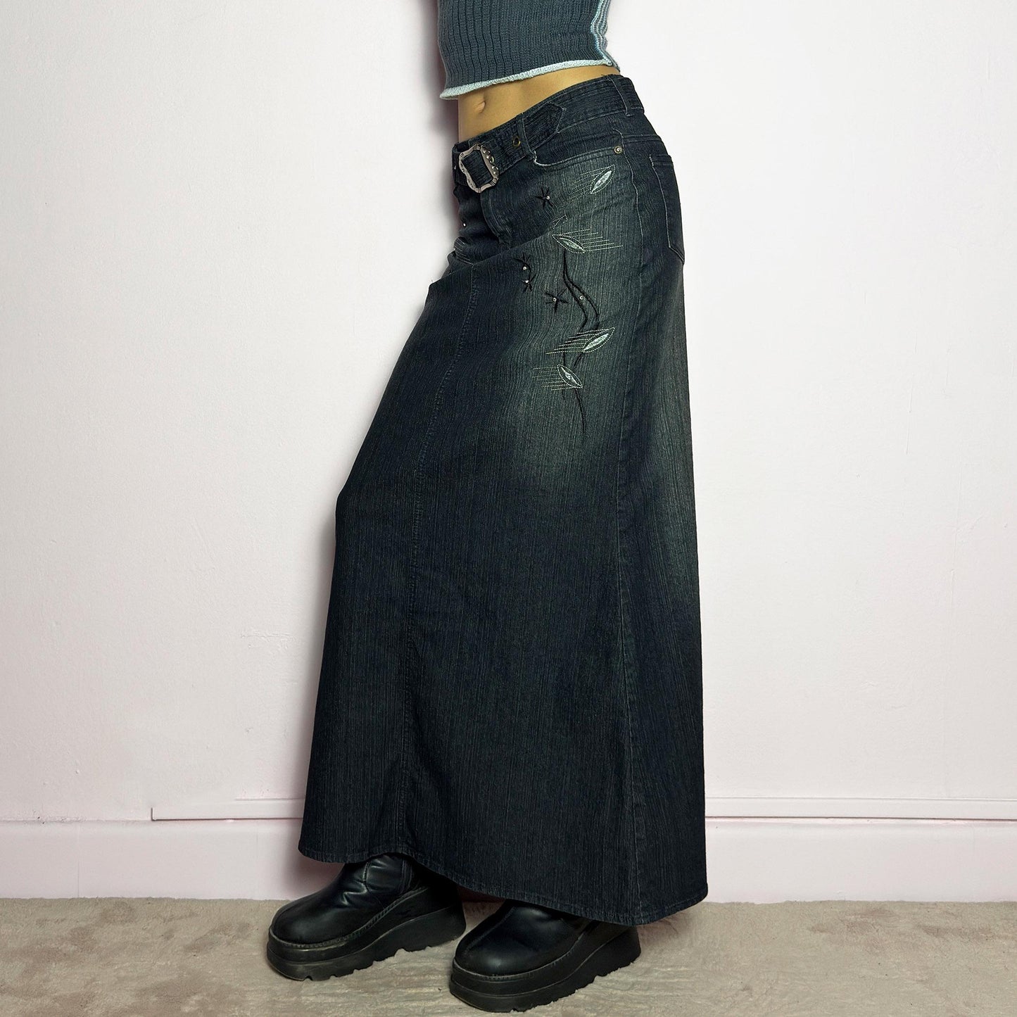 The Y2K Black Denim Maxi Skirt is a vintage 2000s piece featuring a sleek dark wash, rhinestone embellishments, and contrast stitching. Designed with a mid-rise fit and a stretchy denim fabric, it offers a structured silhouette that flares at the bottom. The skirt is finished with a button and zipper closure, pockets, and a removable belt for a customizable look. Perfect for casual streetwear outfits or an elegant night out. adult world shop