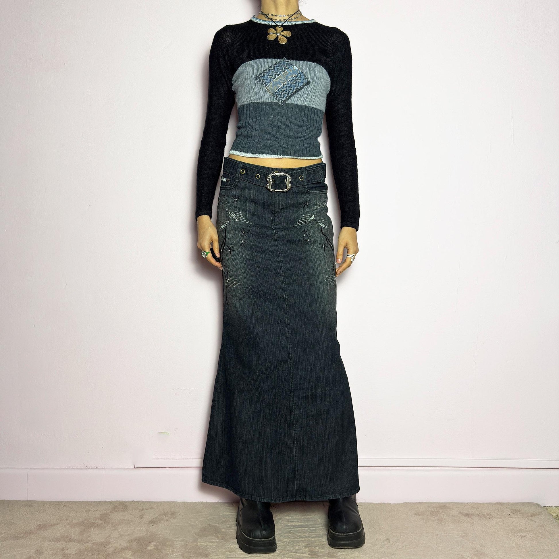 The Y2K Black Denim Maxi Skirt is a vintage 2000s piece featuring a sleek dark wash, rhinestone embellishments, and contrast stitching. Designed with a mid-rise fit and a stretchy denim fabric, it offers a structured silhouette that flares at the bottom. The skirt is finished with a button and zipper closure, pockets, and a removable belt for a customizable look. Perfect for casual streetwear outfits or an elegant night out. adult world shop
