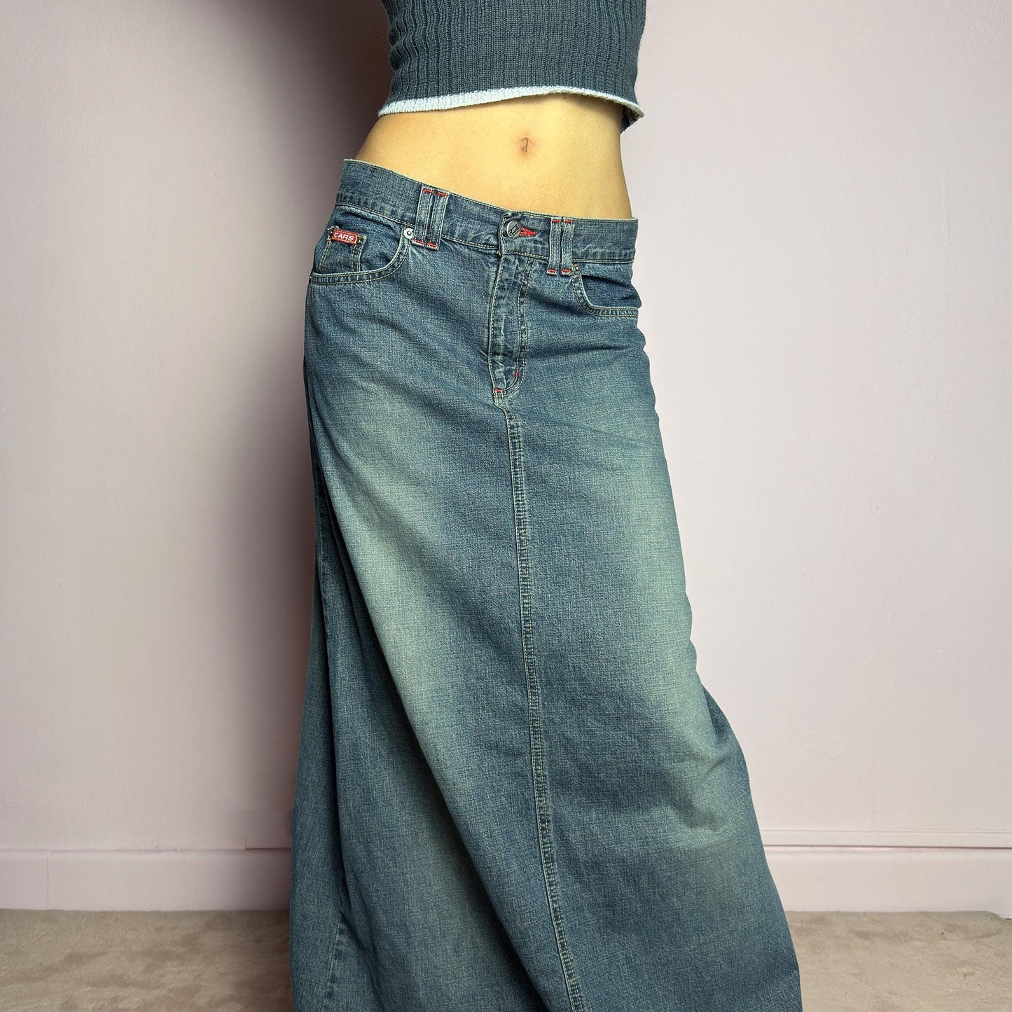 The Y2K Denim Maxi Skirt is a vintage 2000s essential featuring a structured denim fabric in a classic blue wash with subtle fading details. Designed with a mid-rise fit, button and zipper closure, and functional pockets, this skirt offers a sleek yet relaxed silhouette. The back slit adds ease of movement, making it perfect for casual everyday wear. adult world shop