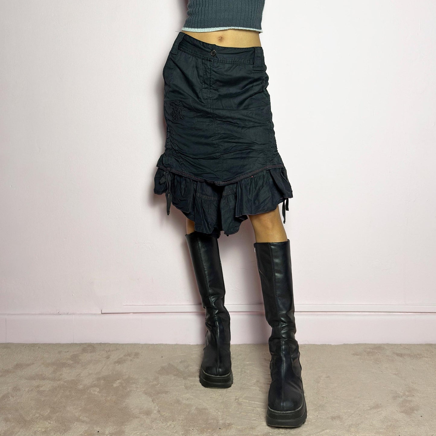 The Y2K Black Layered Skirt by Marithé François Girbaud is a vintage 2000s statement piece featuring a structured design with ruched details and ruffled layers for added texture and movement. Designed with a mid-rise fit, button and zipper closure, embroidered side detail, and an asymmetrical hem, this skirt blends edgy streetwear vibes with a playful, gothic aesthetic. Perfect for casual grunge and alternative looks. adult world shop