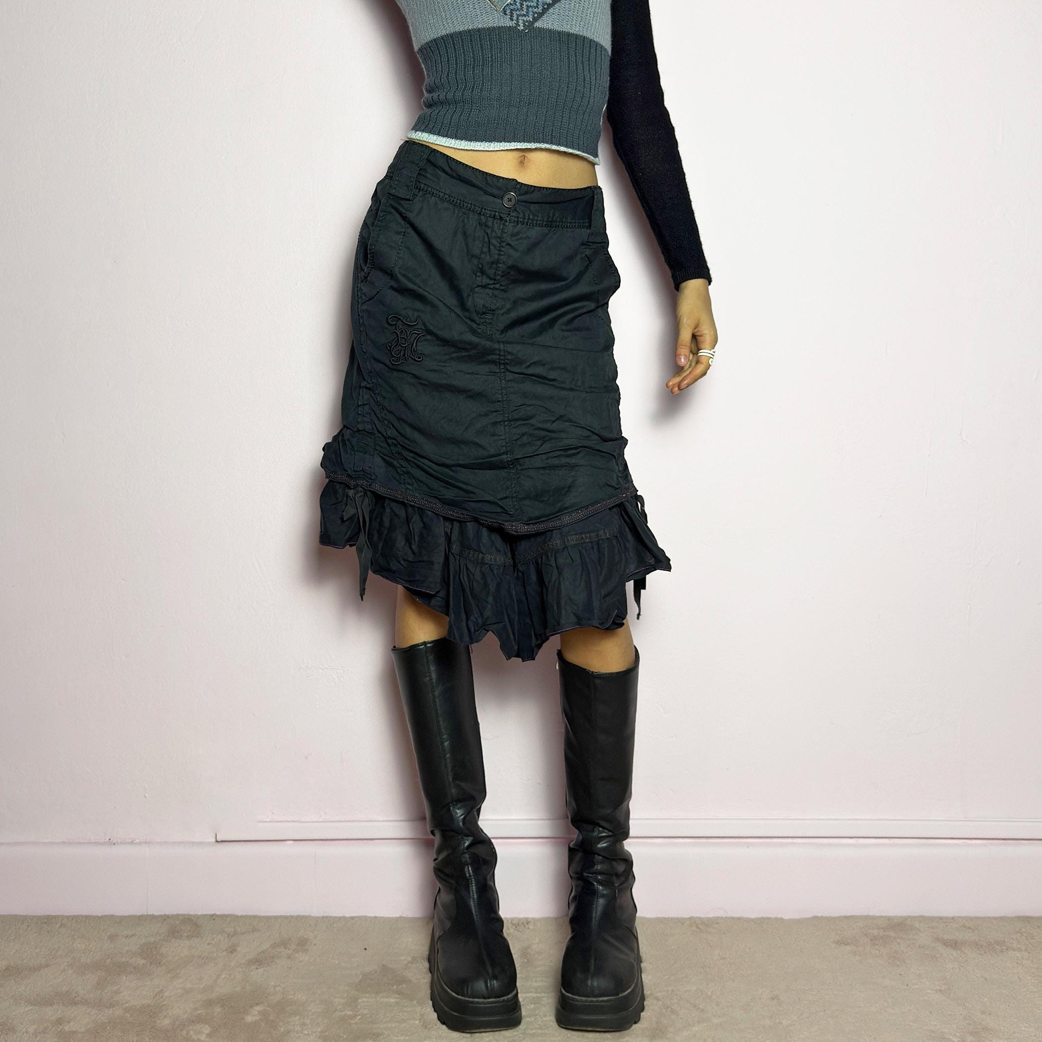 The Y2K Black Layered Skirt by Marithé François Girbaud is a vintage 2000s statement piece featuring a structured design with ruched details and ruffled layers for added texture and movement. Designed with a mid-rise fit, button and zipper closure, embroidered side detail, and an asymmetrical hem, this skirt blends edgy streetwear vibes with a playful, gothic aesthetic. Perfect for casual grunge and alternative looks. adult world shop