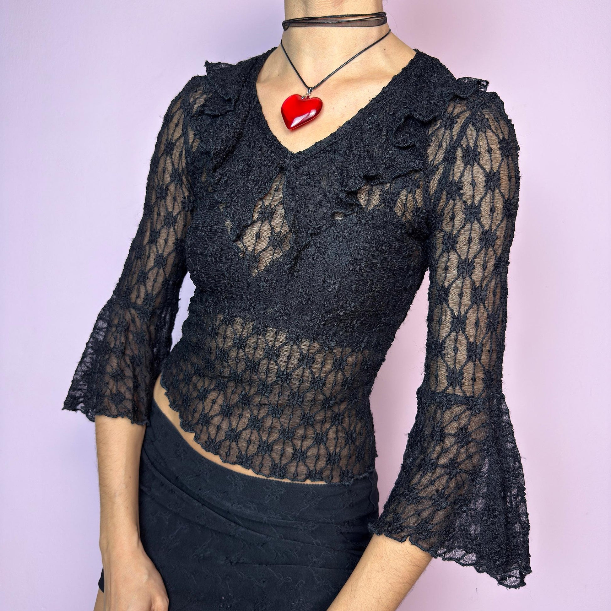 The Y2K Lace Ruffle Black Top is a vintage 2000s sheer black lace top featuring a fitted silhouette, mini ruffle details along the neckline, and flared three-quarter bell sleeves. The textured floral lace adds a romantic gothic touch, perfect for layering or wearing on its own. Ideal for summer night looks and festival outfits. Great vintage condition. adult world shop