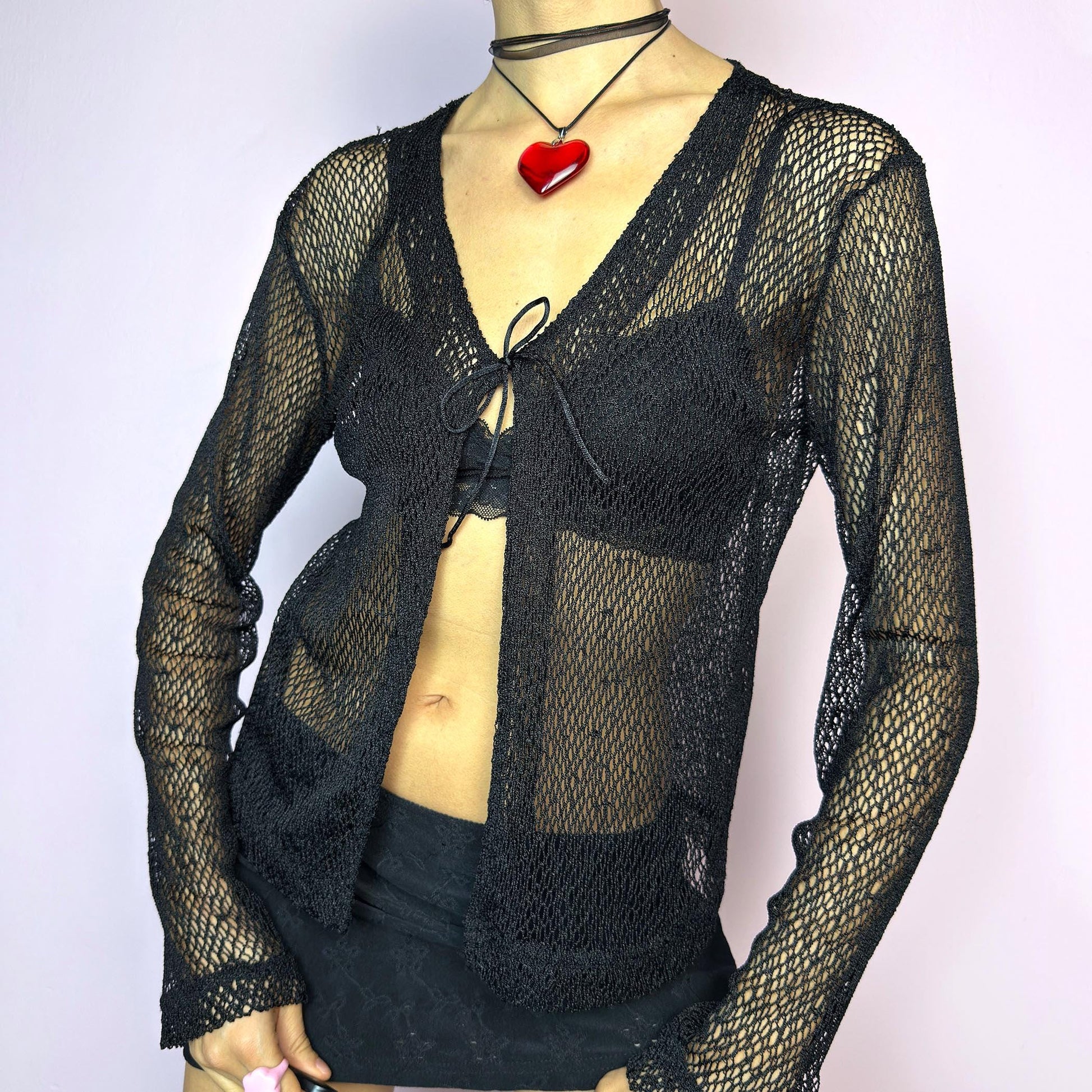The Y2K Black Sheer Tie Top is a vintage 2000s sheer tie-front top in a bold black fishnet knit. Features a breathable, lightweight mesh texture with long sleeves and a single front tie for an adjustable fit. The open weave adds an edgy, see-through effect — ideal for layering. A perfect festival piece and summer staple. Great vintage condition. adult world shop