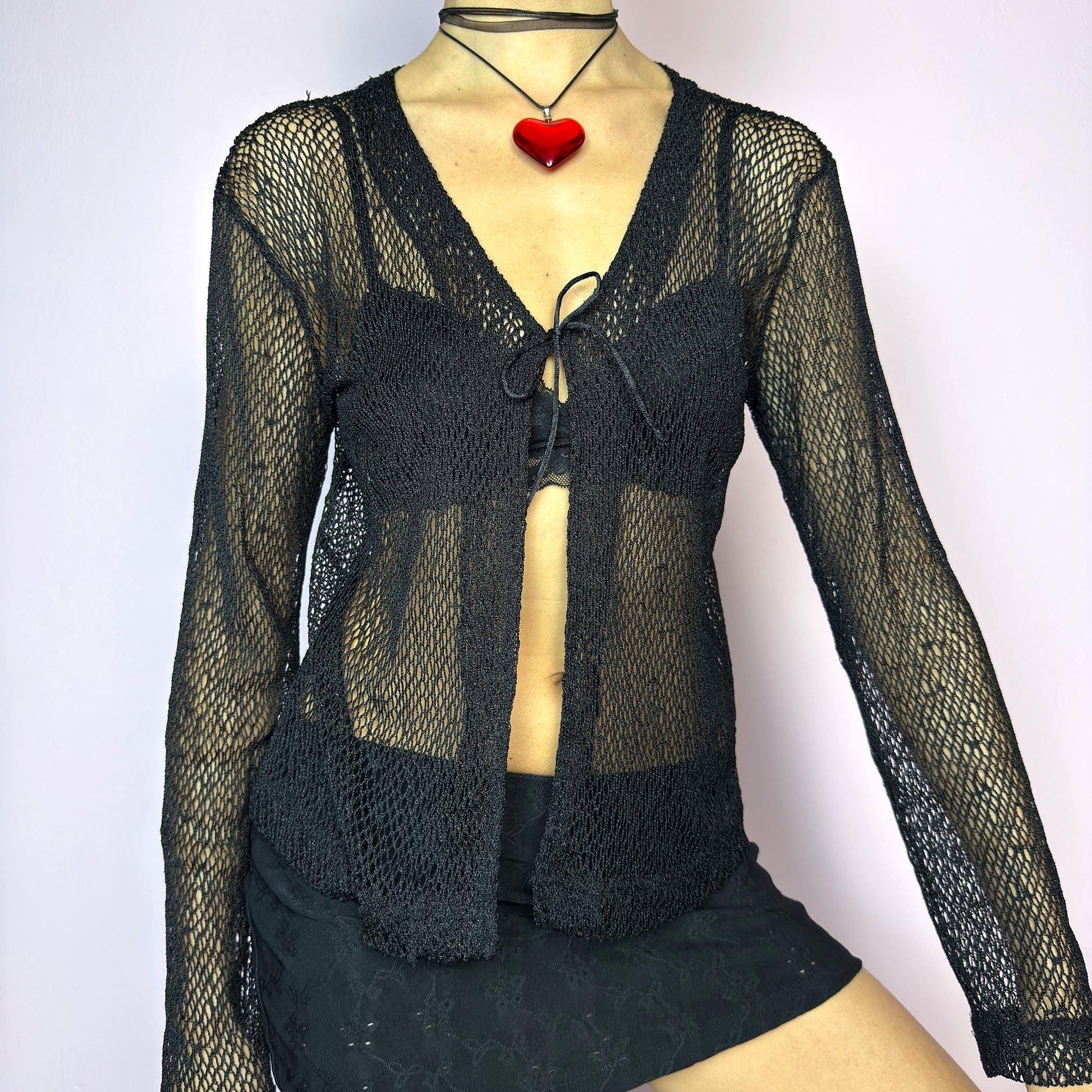 The Y2K Black Sheer Tie Top is a vintage 2000s sheer tie-front top in a bold black fishnet knit. Features a breathable, lightweight mesh texture with long sleeves and a single front tie for an adjustable fit. The open weave adds an edgy, see-through effect — ideal for layering. A perfect festival piece and summer staple. Great vintage condition. adult world shop