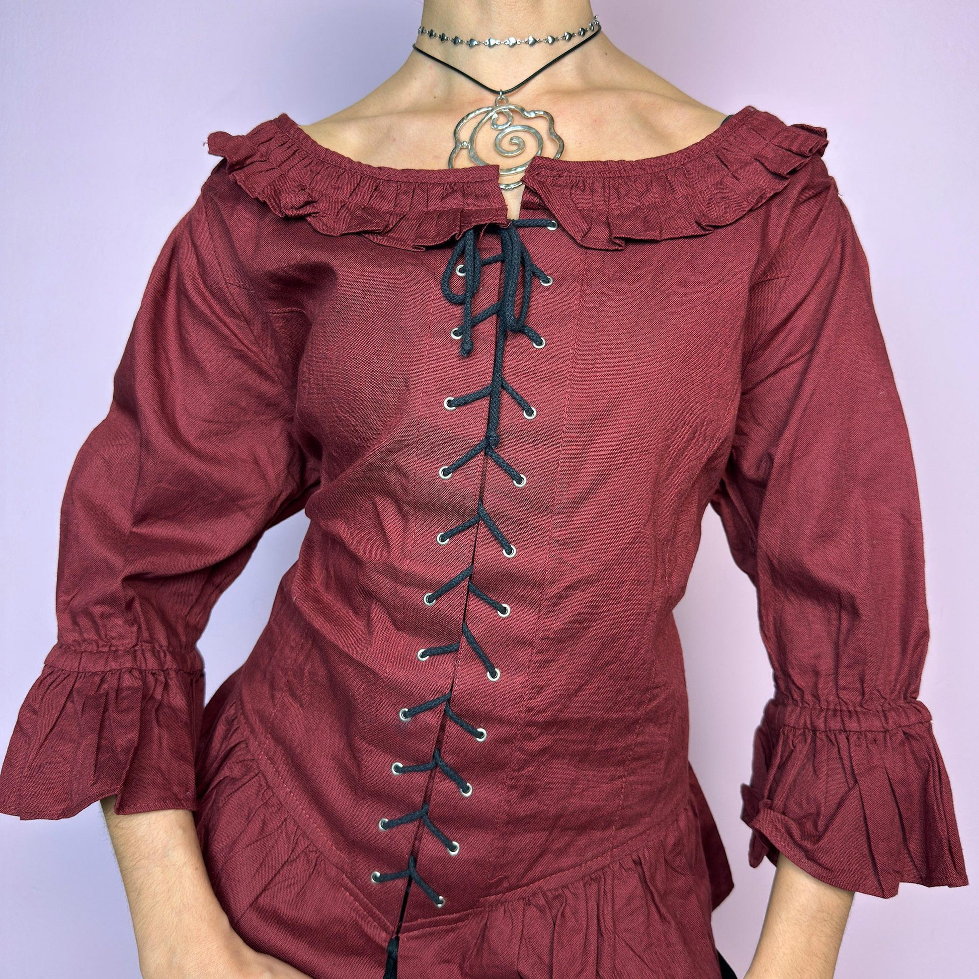 The Vintage 90s Maroon Lace Up Top is a romantic and dramatic piece inspired by gothic and cottagecore aesthetics. Crafted in a deep wine red tone, it features front and back corset-style lace-up details for an adjustable fit. The design includes a ruffled off-the-shoulder neckline, voluminous three-quarter sleeves with gathered ruffle cuffs, and a flattering cinched waist with a ruffled hem. Perfect for creating fairytale-inspired outfits or statement festival looks. adult world shop
