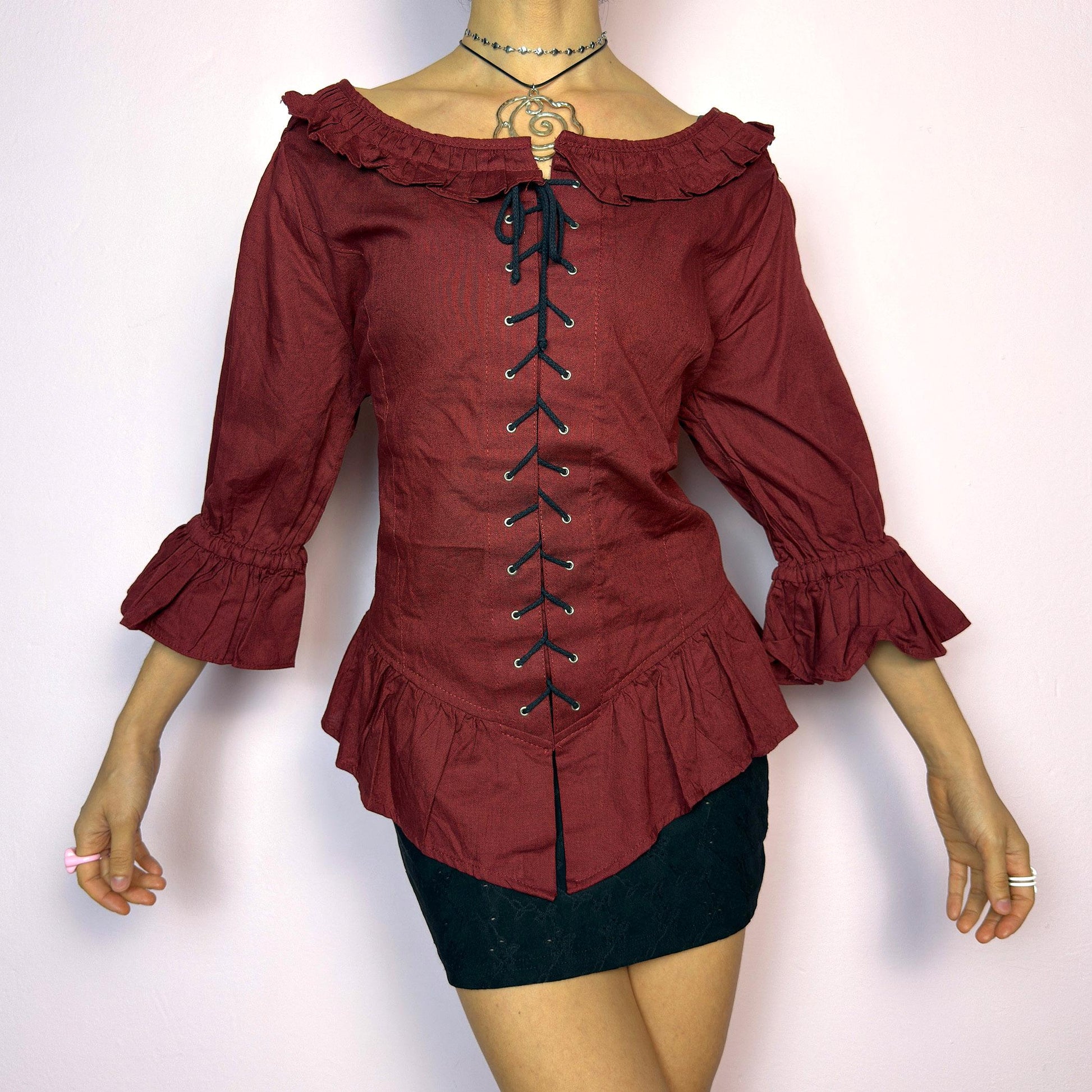 The Vintage 90s Maroon Lace Up Top is a romantic and dramatic piece inspired by gothic and cottagecore aesthetics. Crafted in a deep wine red tone, it features front and back corset-style lace-up details for an adjustable fit. The design includes a ruffled off-the-shoulder neckline, voluminous three-quarter sleeves with gathered ruffle cuffs, and a flattering cinched waist with a ruffled hem. Perfect for creating fairytale-inspired outfits or statement festival looks. adult world shop