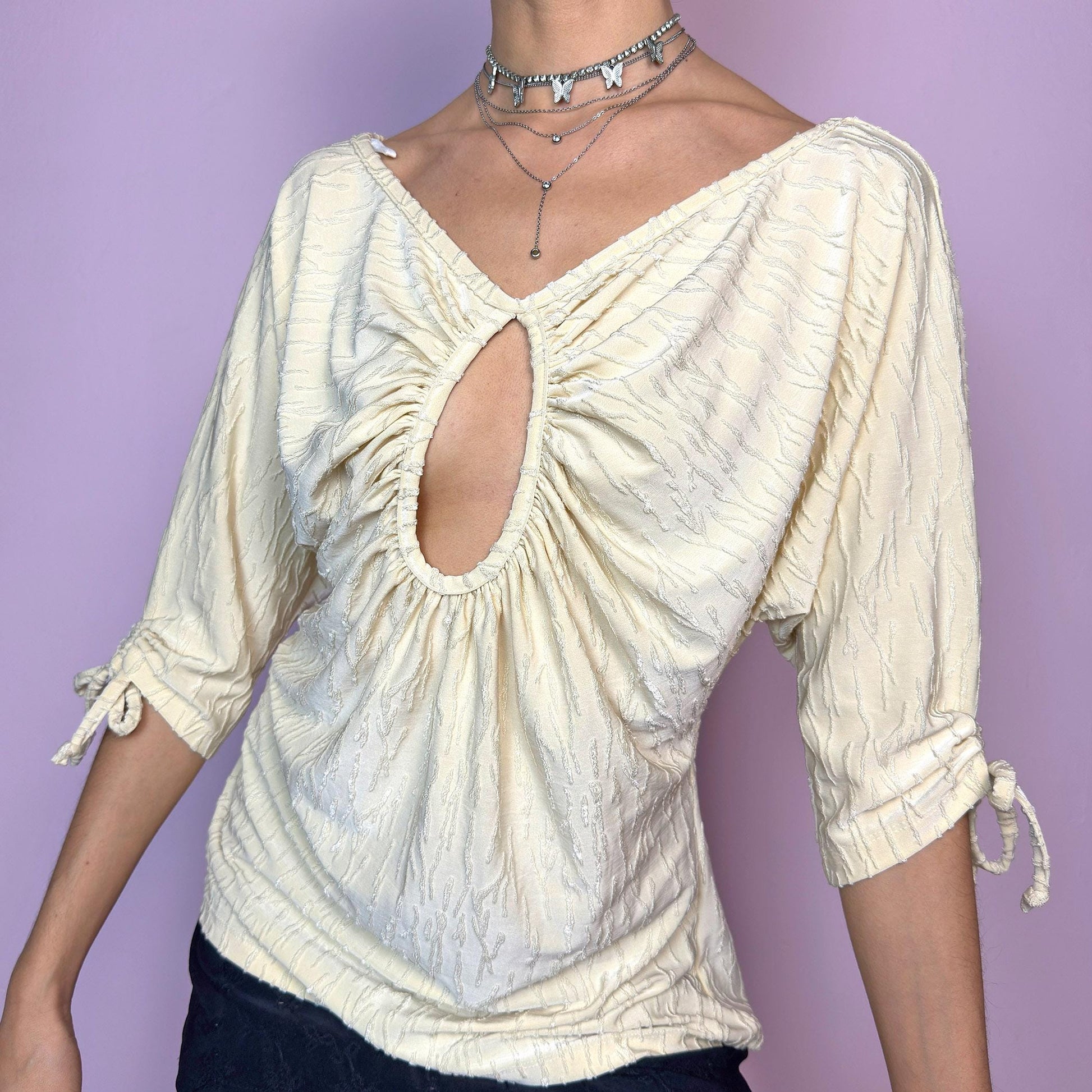 The Y2K Ruched Keyhole Top is a vintage 2000s piece crafted from a textured, stretchy fabric in a pale yellowish cream tone. Features a flattering gathered bust with a keyhole cutout, V-neckline, and soft drape. The three-quarter sleeves are finished with delicate tie details for an adjustable fit. Perfect for summer days and casual dates. Made in Spain. Excellent vintage condition. adult world shop