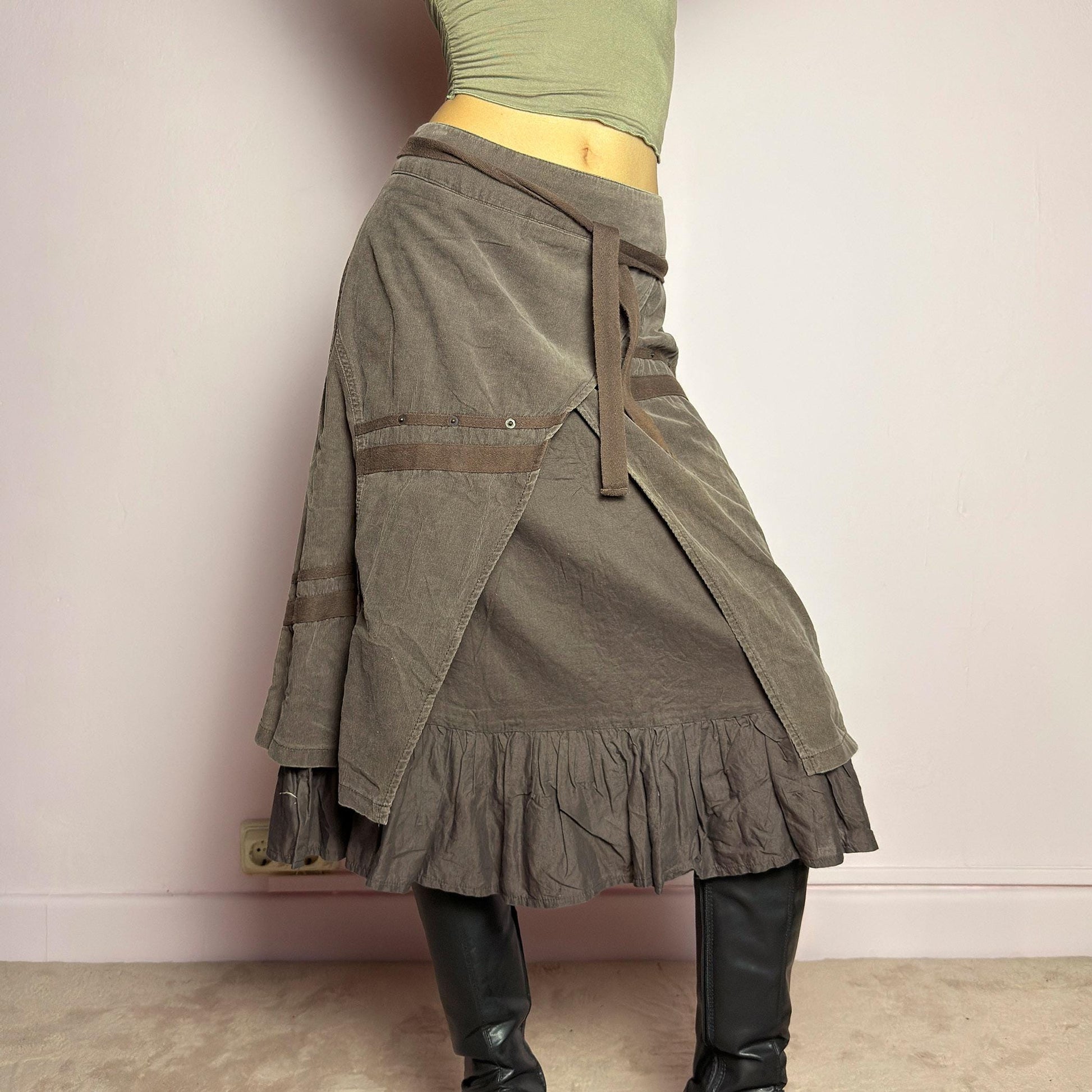 The Y2K Layered Brown Midi Skirt is a unique vintage 2000s piece featuring an asymmetric wrap design with a layered ruffle hem. Made from corduroy-cotton fabric, it includes tie closures for an adjustable fit, a back zipper closure, and subtle stitched detailing that adds a deconstructed touch. Perfect for earthy, bohemian, or avant-garde styling. adult world shop