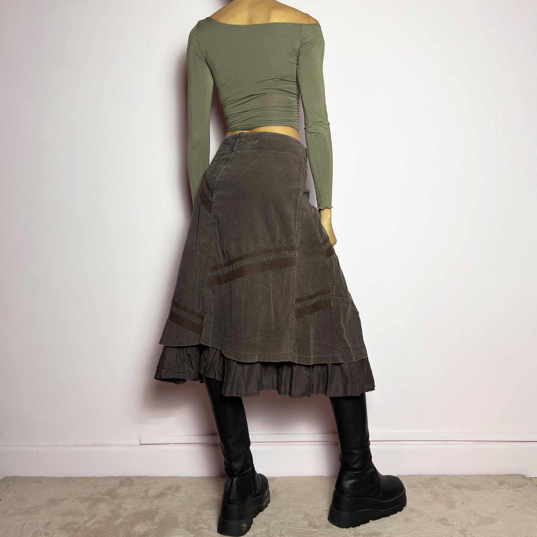The Y2K Layered Brown Midi Skirt is a unique vintage 2000s piece featuring an asymmetric wrap design with a layered ruffle hem. Made from corduroy-cotton fabric, it includes tie closures for an adjustable fit, a back zipper closure, and subtle stitched detailing that adds a deconstructed touch. Perfect for earthy, bohemian, or avant-garde styling. adult world shop