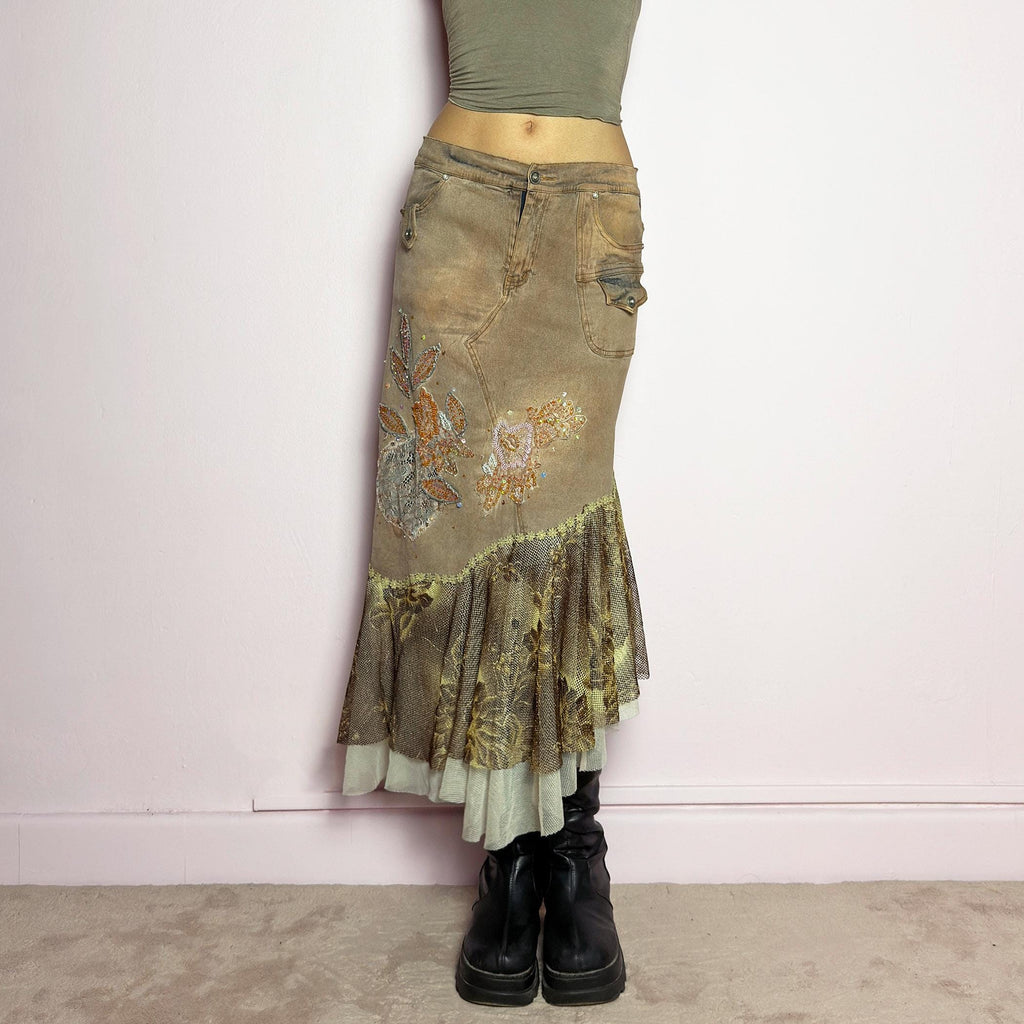 The Y2K Asymmetric Ruffle Midi Skirt is a vintage 2000s statement piece featuring a stretchy distressed tan denim base adorned with intricate beaded floral embroidery and sequin details. Designed with an asymmetric layered ruffle hem made of sheer lace and mesh with a metallic floral pattern, this skirt creates a dreamy, deconstructed aesthetic. It includes a button and zipper closure, belt loops, and pockets. adult world shop