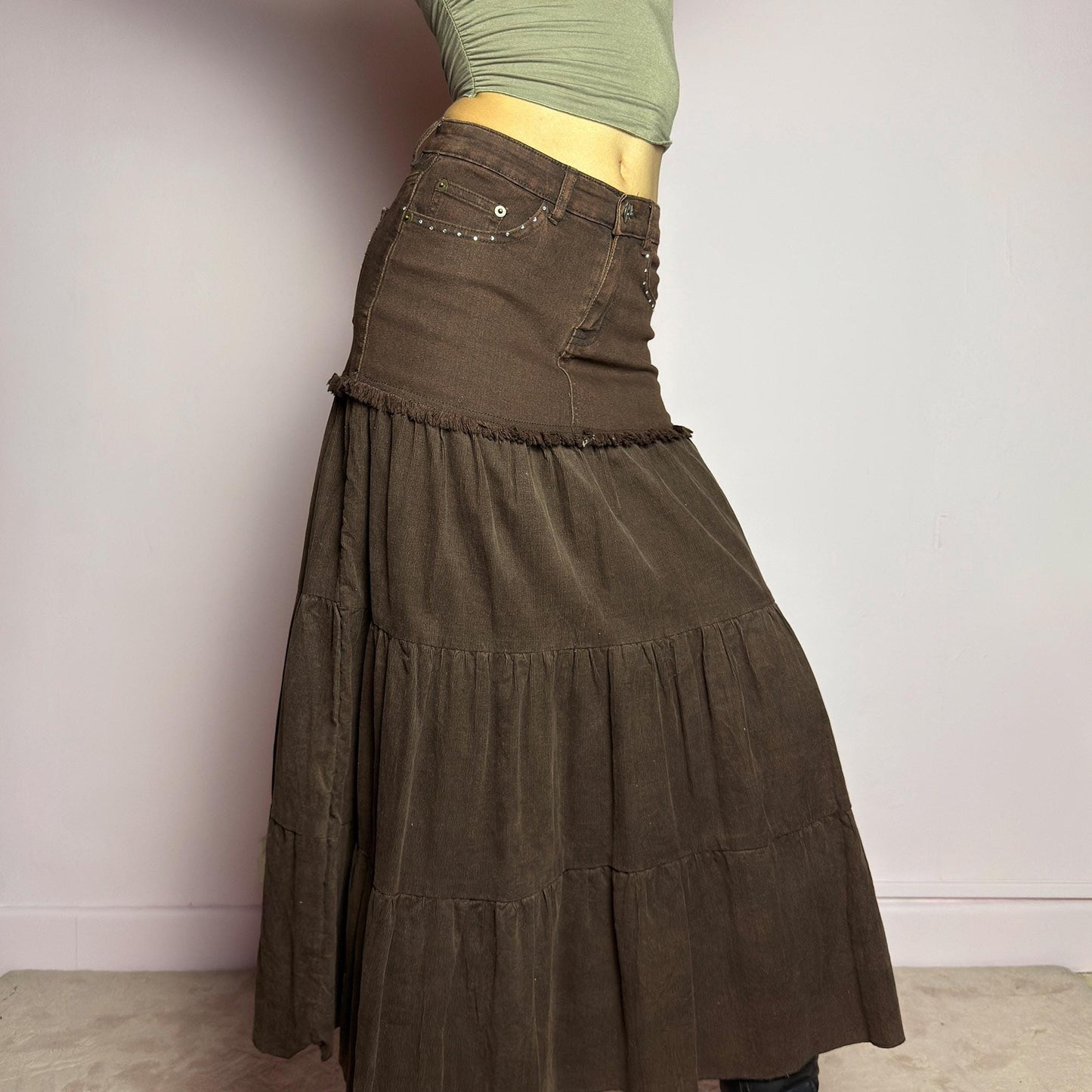 The Y2K Brown Tiered Midi Skirt is a vintage 2000s piece combining denim and soft corduroy for a unique mixed-fabric look. Featuring a stretchy waistband with rhinestone embellishments, pockets and a button-zipper closure, this skirt transitions into flowy tiered corduroy panels for a boho-inspired silhouette. Perfect for casual outfits. adult world shop