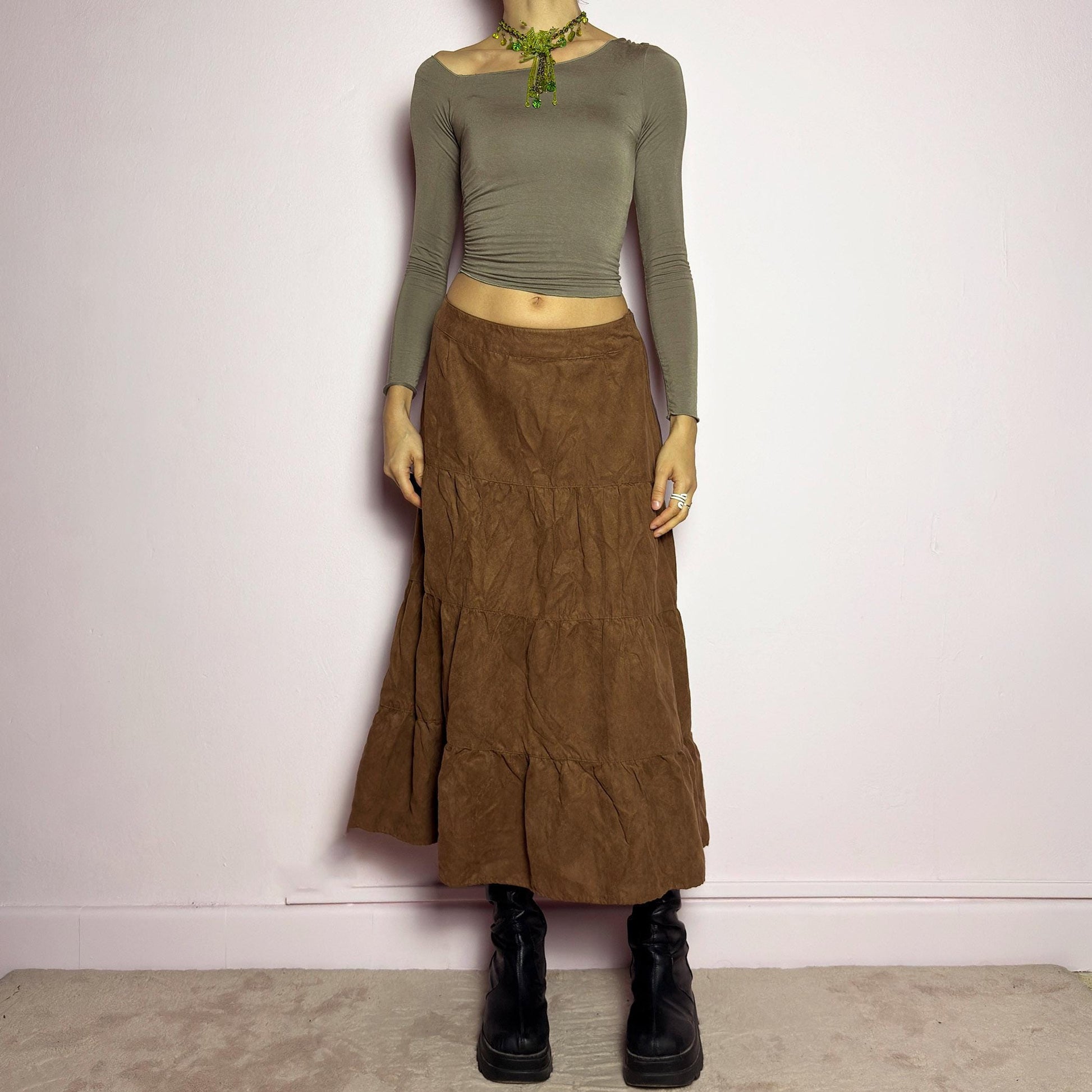 The Y2K Tiered Brown Midi Skirt is a vintage 2000s piece featuring a soft faux suede style fabric. Designed with a voluminous tiered structure for a flowy silhouette and a side zipper closure, this skirt has a mid-rise fit and an earthy brown tone, perfect for bohemian or casual outfits. adult world shop