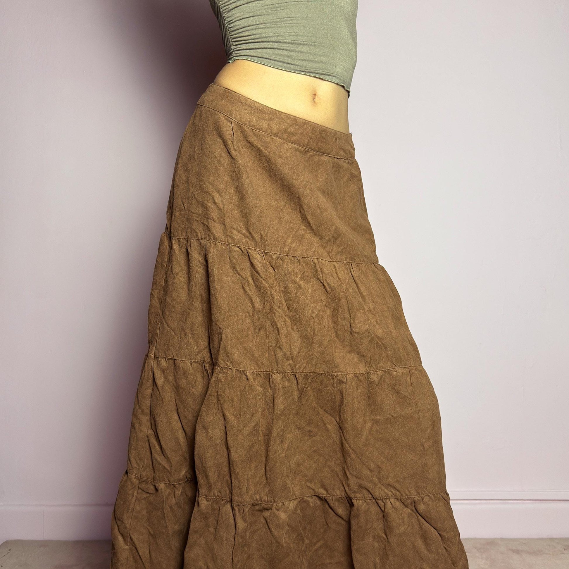 The Y2K Tiered Brown Midi Skirt is a vintage 2000s piece featuring a soft faux suede style fabric. Designed with a voluminous tiered structure for a flowy silhouette and a side zipper closure, this skirt has a mid-rise fit and an earthy brown tone, perfect for bohemian or casual outfits. adult world shop