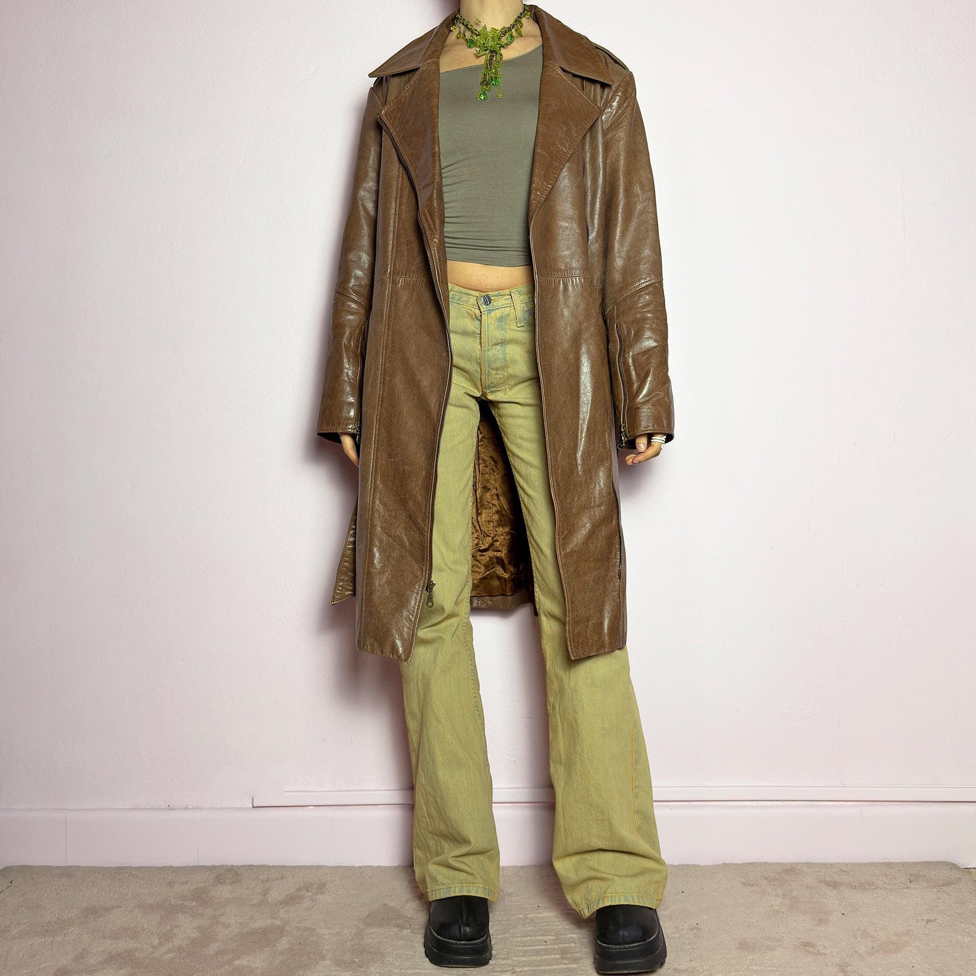 The Y2K Long Brown Leather Coat is a heavy, structured vintage 2000s piece crafted from genuine leather. It features an asymmetrical zip closure, a wide lapel collar, and a belted waist for a cinched silhouette. The coat includes pockets and a smooth lining for comfort. With its durable construction and timeless design, this vintage long leather coat is perfect for edgy streetwear or sophisticated layering. adult world shop