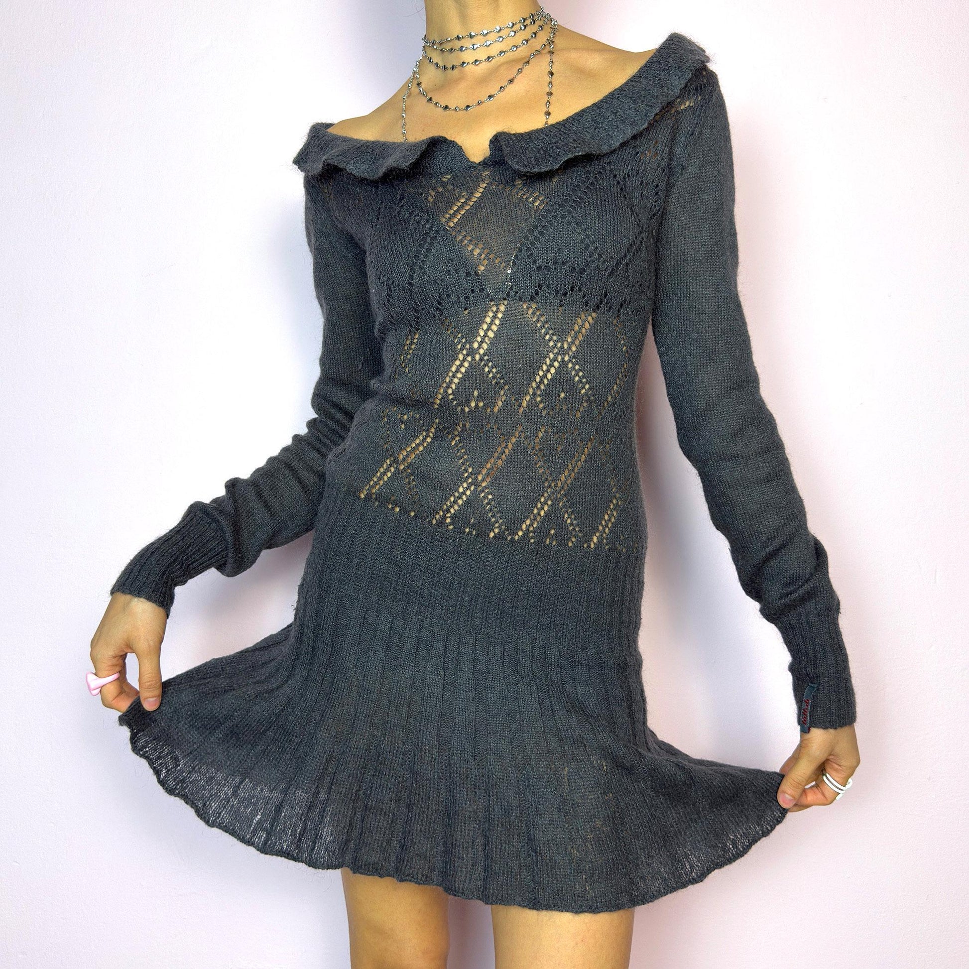The Y2K Gray Mini Knit Dress is a vintage 2000s piece featuring a ruffled off-shoulder neckline and sheer diamond-knit pattern through the bodice. The fitted waist flows into a pleated mini skirt. Made from a soft, stretchy knit that hugs the body while remaining comfortable. Perfect for casual autumn look. adult world shop