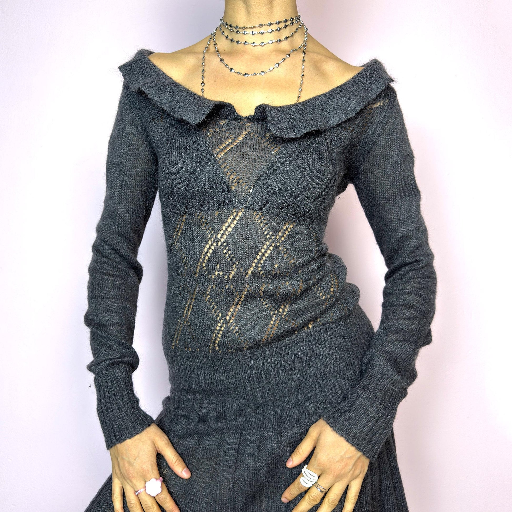 The Y2K Gray Mini Knit Dress is a vintage 2000s piece featuring a ruffled off-shoulder neckline and sheer diamond-knit pattern through the bodice. The fitted waist flows into a pleated mini skirt. Made from a soft, stretchy knit that hugs the body while remaining comfortable. Perfect for casual autumn look. adult world shop
