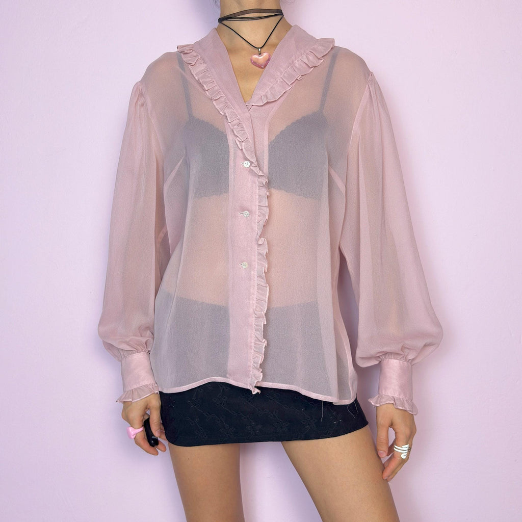 The Vintage Pink Ruffle Sheer Blouse features a romantic and ethereal silhouette with soft, see-through fabric and delicate ruffle trim along the collar and button placket. The flowy cut and voluminous sleeves with buttoned cuffs add a dreamy charm. Perfect for layering for a soft coquette aesthetic. Made in France. Excellent vintage condition. adult world shop