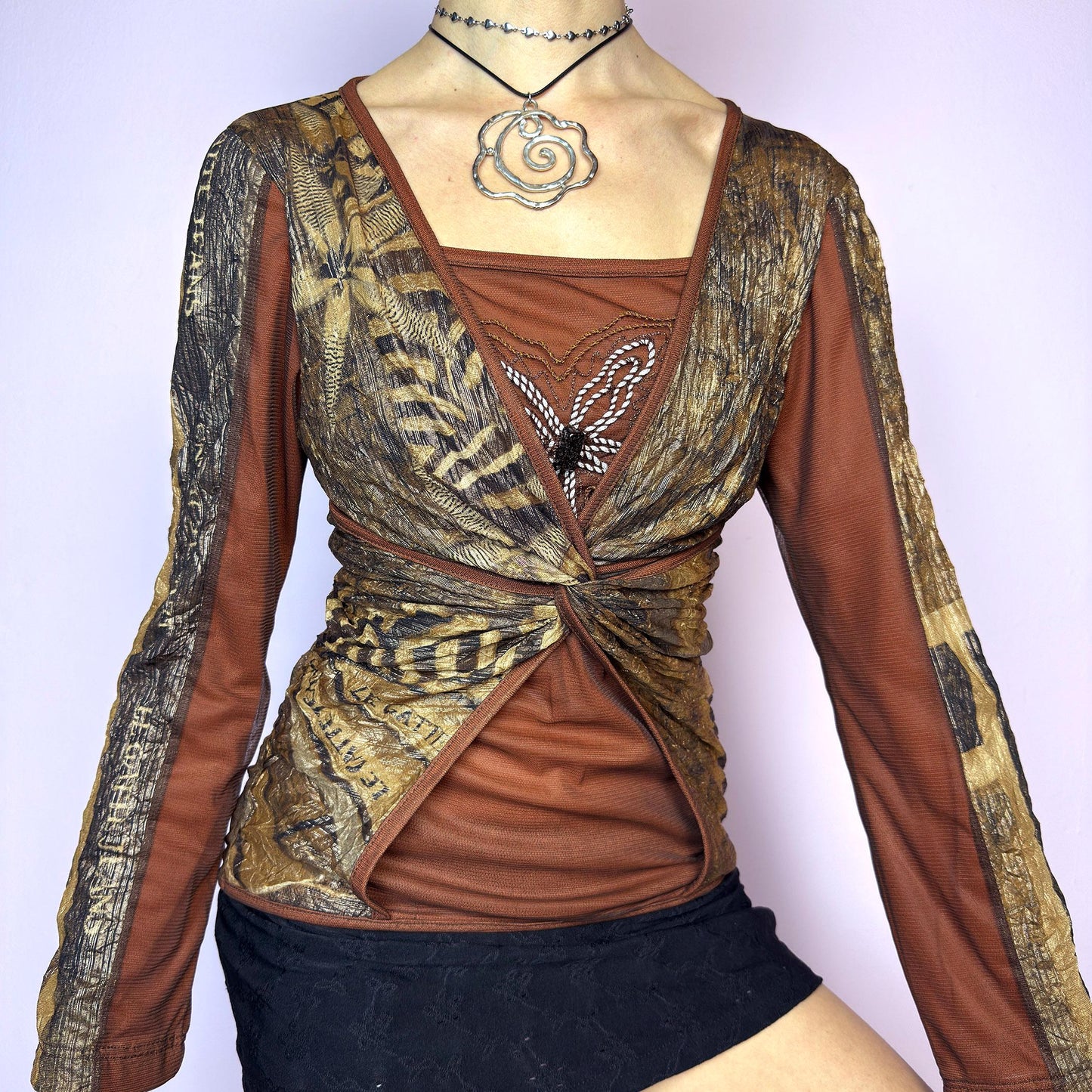 The Y2K Brown Mesh Overlay Top is a vintage 2000s long sleeve designed by Legatte Jeans. Crafted in a moody mix of orange, brown, and bronze tones, it features a twisted front detail and a combination of stretchy mesh and jersey fabrics. A subtle embroidered flower motif decorates the chest, adding a delicate accent to the bold, structured silhouette. With its sculptural cut and sheer elements, this top is perfect for cyber aesthetics, artsy fashion, and Y2K clubwear. adult world shop