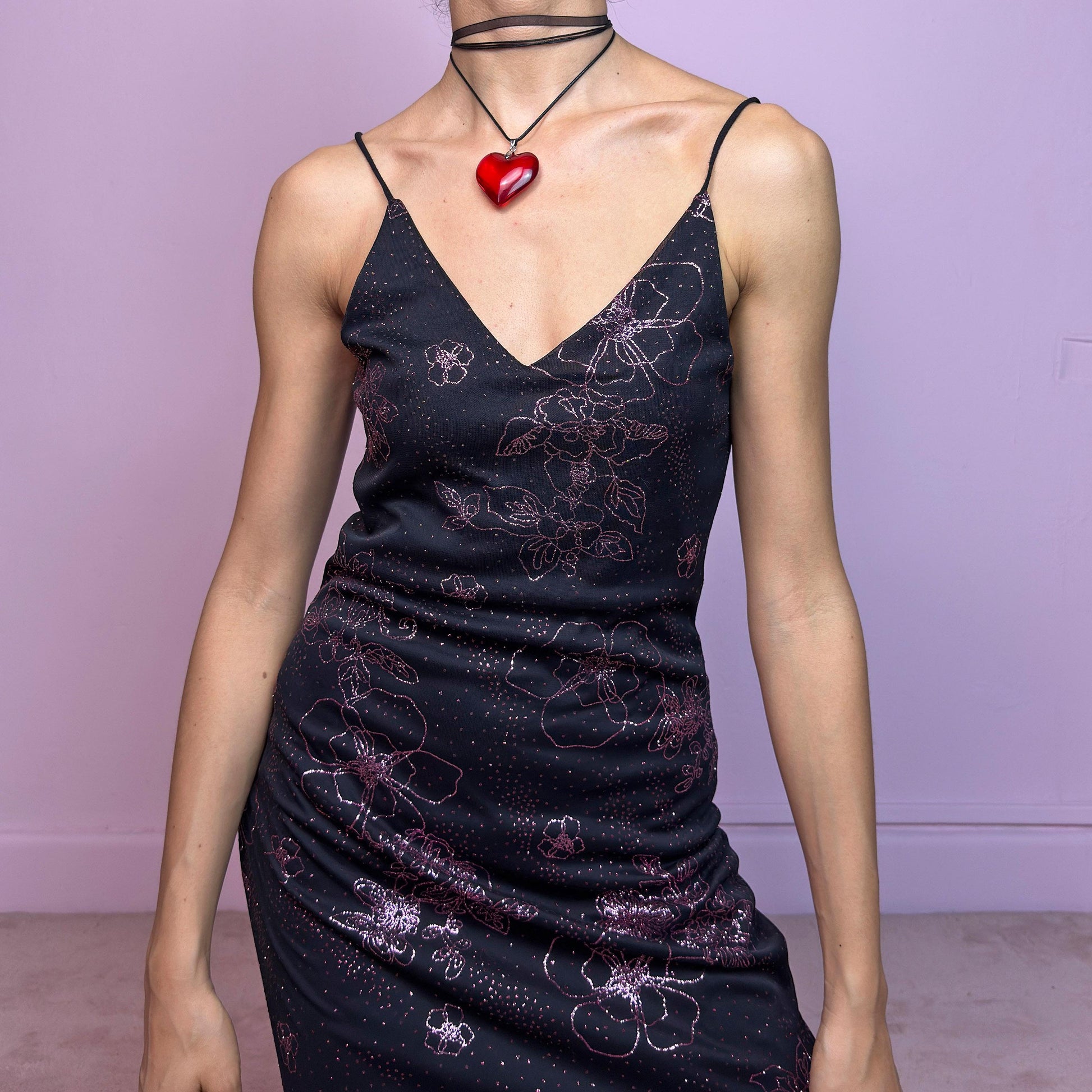 The Y2K Black Glitter Midi Dress is a rare 2000s dress featuring a delicate pink glitter floral pattern on a sheer black mesh overlay with a soft lining beneath. This midi-length piece includes skinny spaghetti straps, a deep V neckline, and a side slits for added movement. The open lace-up back detail gives it a sultry edge, perfect for night outs, alt party looks, or romantic goth aesthetics. Fitted silhouette with a flattering drape. Made in France. Excellent vintage condition.