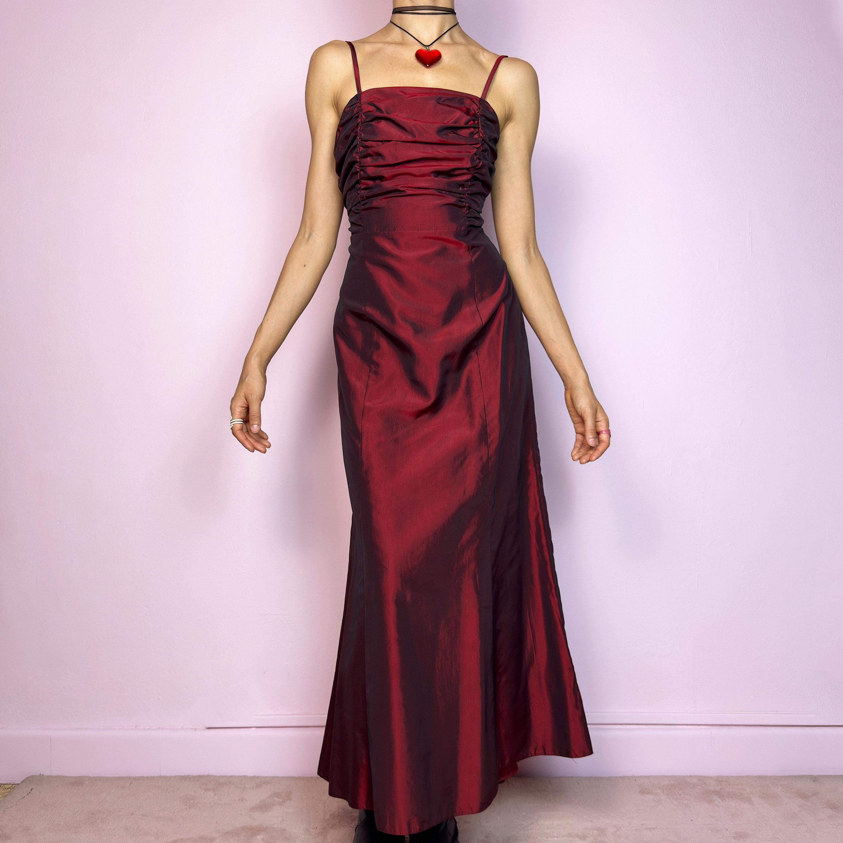The Vintage 90s Burgundy Ruched Maxi Dress is a show-stopping piece featuring a rich burgundy tone with a lustrous satin-style finish. The ruched bodice adds texture and dimension, while the fitted silhouette flows into a soft A-line skirt. Designed with dainty spaghetti straps, a maxi length for dramatic flair, and a hidden side zipper closure for a seamless fit. Perfect for prom, formal events, or romantic night-outs. Excellent vintage condition.