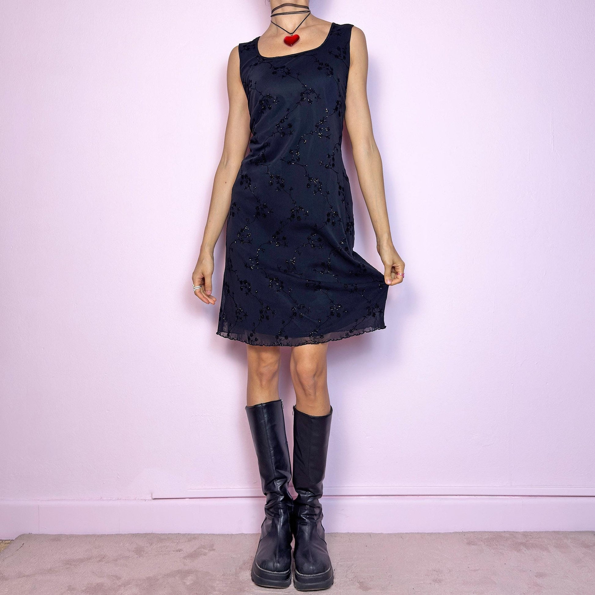The Vintage 90s Black Mesh Mini Dress is a delicate and stretchy black mini dress featuring sheer mesh overlay with velvet floral embroidery and subtle glitter accents. Designed with a flattering sleeveless silhouette, scoop neckline, and lettuce hem for a soft romantic touch. Perfect for witchy party looks, 90s glam nights, or layering with grunge accessories. Made in UK. Excellent vintage condition.