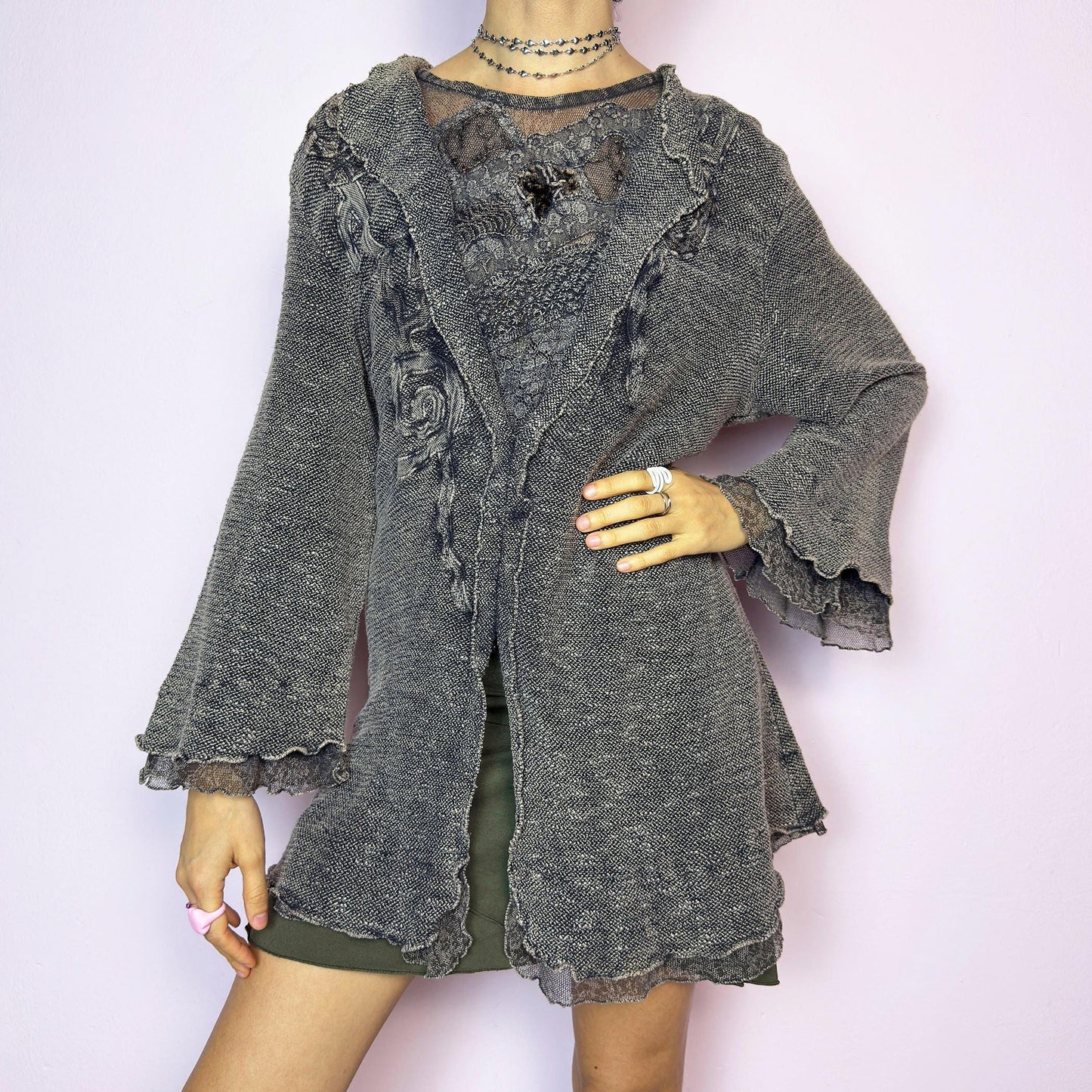 The Vintage 90s Medieval Ruffle Knit Top is a rare and enchanting piece with rustic, fairycore charm. Made from thick textured knit in a washed charcoal hue, it features flared three-quarter sleeves, ruffled lace trim, and intricate appliqué embroidery details. The open split front and ruffled hem bring a dramatic, medieval-inspired silhouette. Perfect for layering with romantic, witchy, or dark cottagecore outfits. Made in Italy. Great vintage condition.