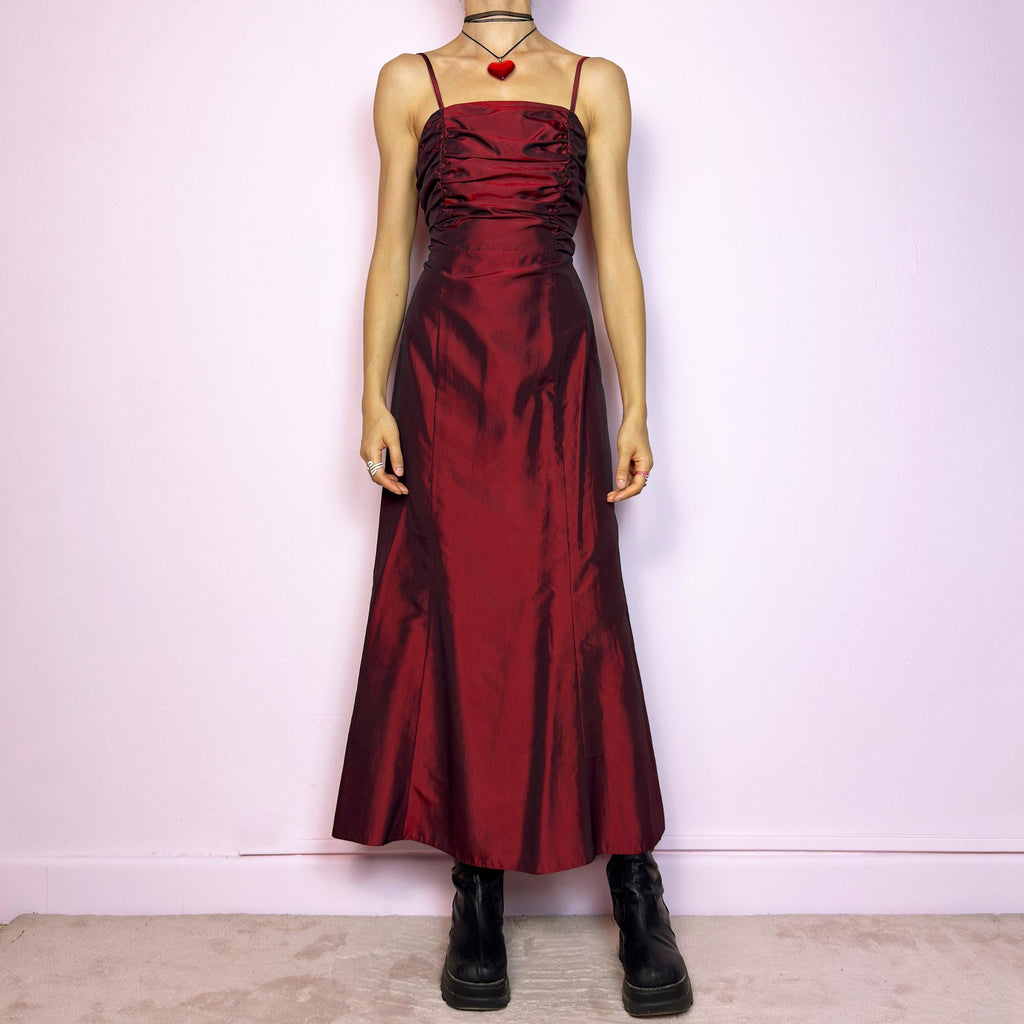 The Vintage 90s Burgundy Ruched Maxi Dress is a show-stopping piece featuring a rich burgundy tone with a lustrous satin-style finish. The ruched bodice adds texture and dimension, while the fitted silhouette flows into a soft A-line skirt. Designed with dainty spaghetti straps, a maxi length for dramatic flair, and a hidden side zipper closure for a seamless fit. Perfect for prom, formal events, or romantic night-outs. Excellent vintage condition.