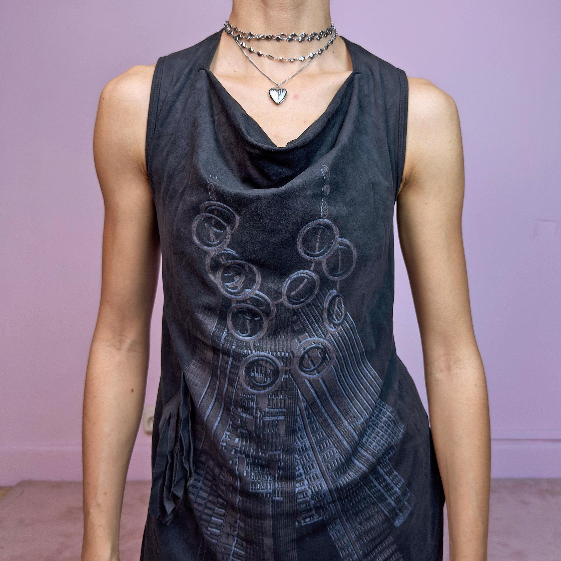 The Y2K Black Asymmetric Mini Dress is a futuristic and artsy vintage 2000s mini dress featuring a unique cowl neckline and layered asymmetric hem. Crafted from soft black stretchy fabric with a subtle suede-like texture, it showcases an abstract tech-inspired print on the front. The sleeveless design and fluid silhouette make it ideal for edgy, experimental, or cyber fairy looks. A true statement piece with avant-garde flair. Excellent vintage condition.