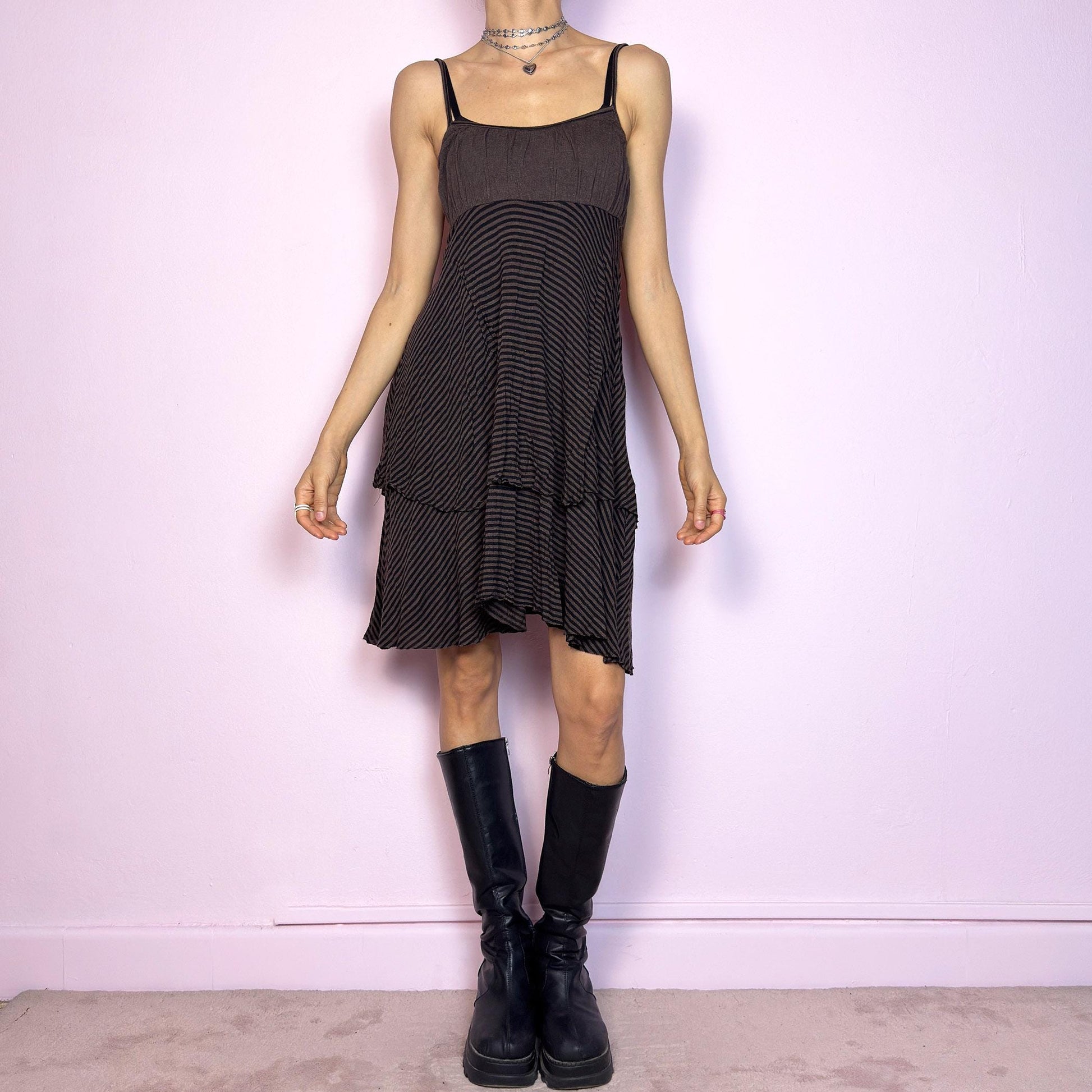 This vintage 2000s brown midi dress features a fine black stripe pattern, square neckline, and thin shoulder straps. Made from a soft, stretchy knit, it has an empire waist and a tiered asymmetric hem that drapes with ease. Perfect for summer. A casual, fairy grunge–inspired piece with subtle volume and flow—blending comfort, minimalism, and quiet edge. Great vintage condition.