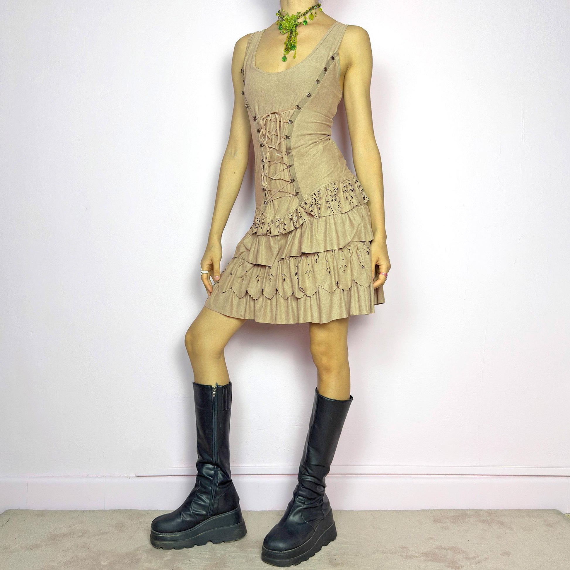 This vintage 2000s mini dress comes in soft beige with a scoop neckline, corset lace-up front, and stretchy fit. The drop waist leads to layered ruffle tiers with eyelet cutouts and scalloped hems. A fairy-meets-western Y2K silhouette—fitted on top, flirty on the bottom. Perfect for casual summer days or standout festival looks. Great vintage condition.