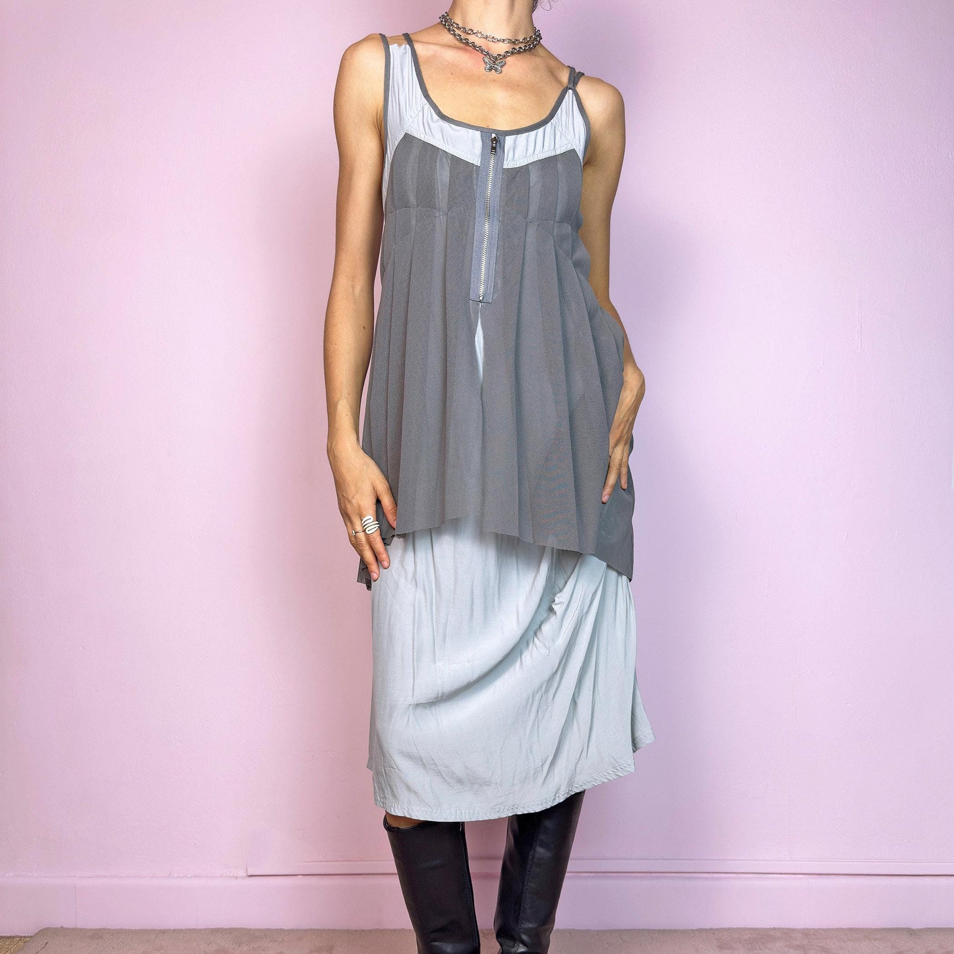 This vintage 2000s midi dress features layered grey tones in mixed textures, including a pleated mesh overlay with faux front zip detail and a side zipper closure. The sleeveless cut and flared asymmetric drape create sculptural movement. Falls below the knee, lightweight, with no stretch. A deconstructed Y2K silhouette—futuristic, quiet, and avant-garde. Perfect for summer days or experimental night looks. Excellent vintage condition.
